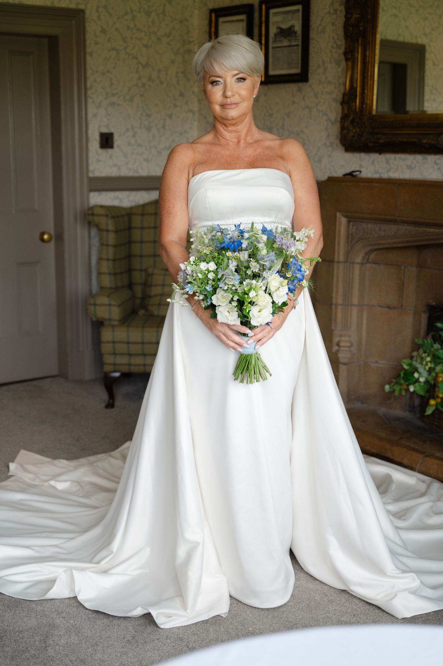 Bride standing indoors holding a bouquet with white, yellow and blue flowers, facing the camera