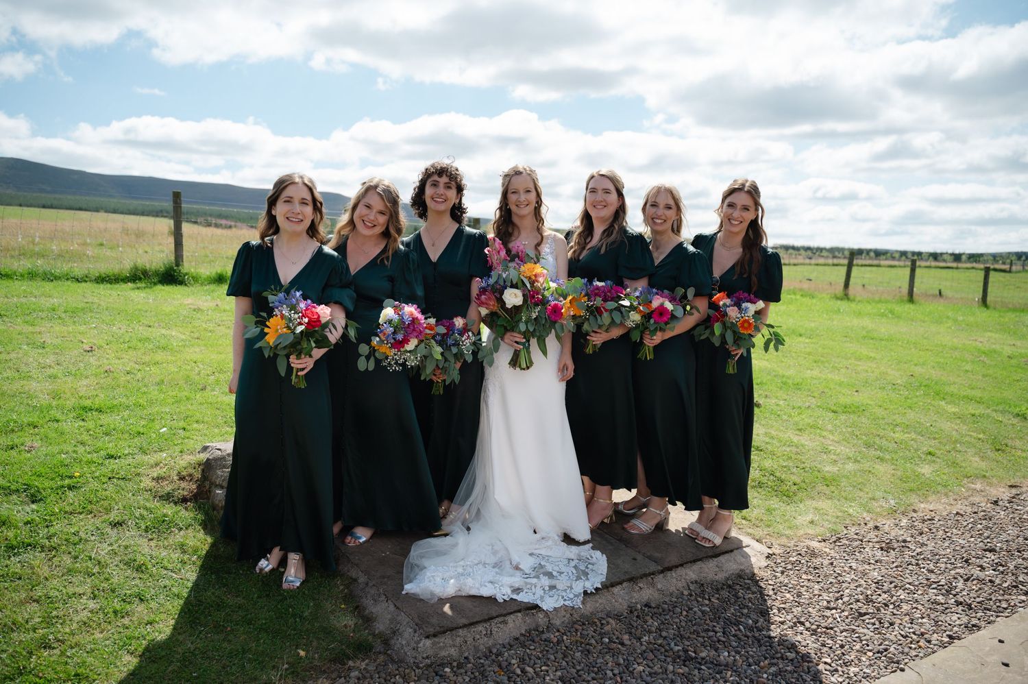 Bride surrounded by bridesmaids in black dresses, all holding colourful bouquets