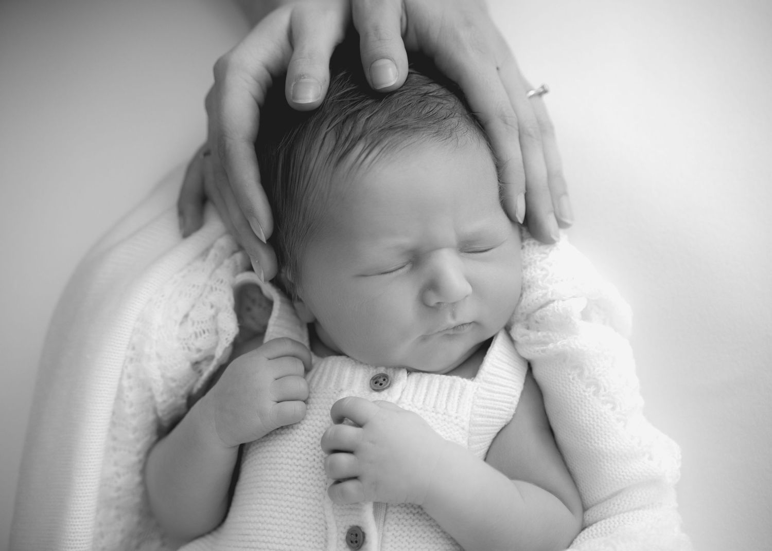 Black and white newborn portrait held gently by a parent’s hands