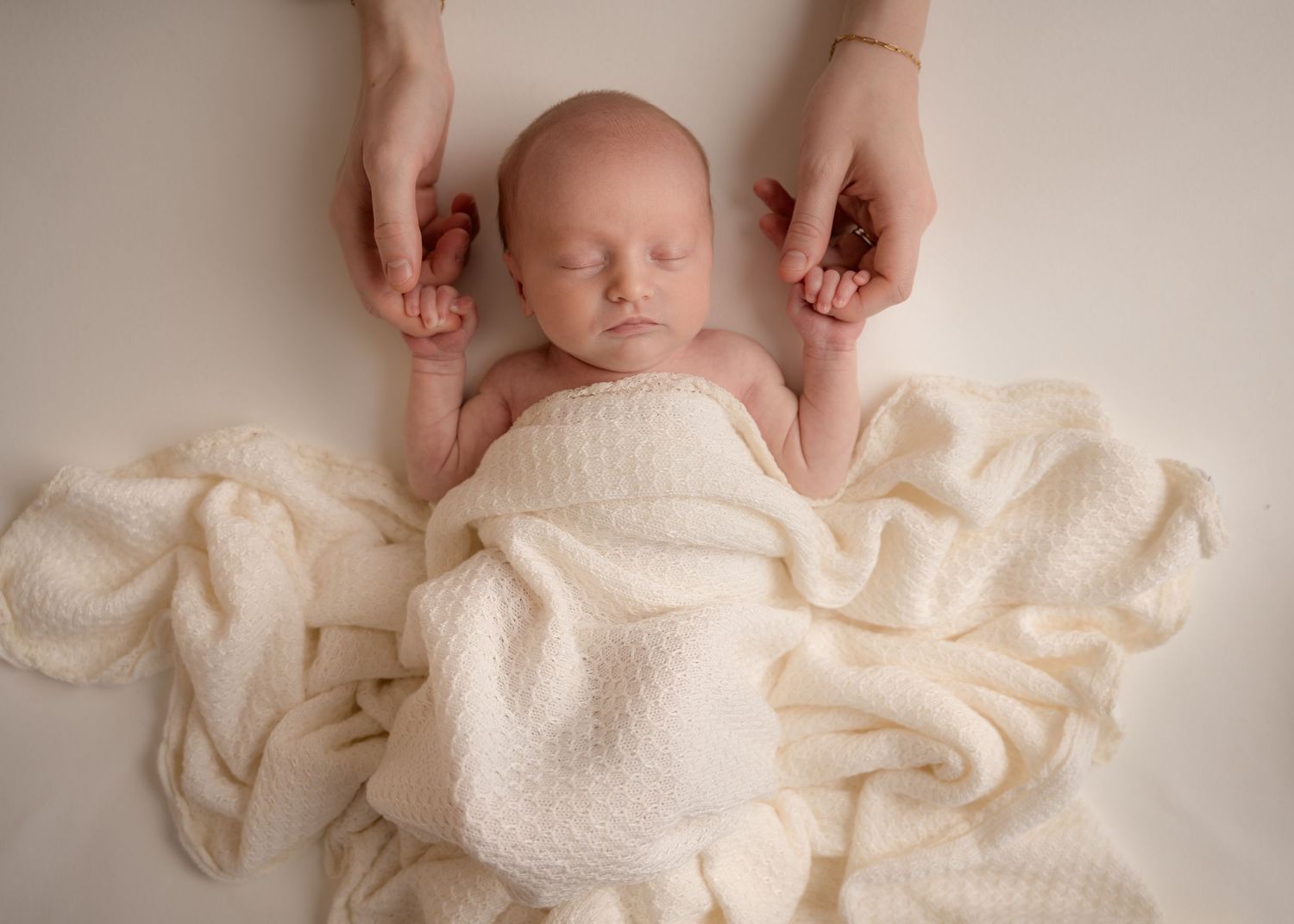 Newborn baby lying on a white blanket with gentle hands adjusting them.