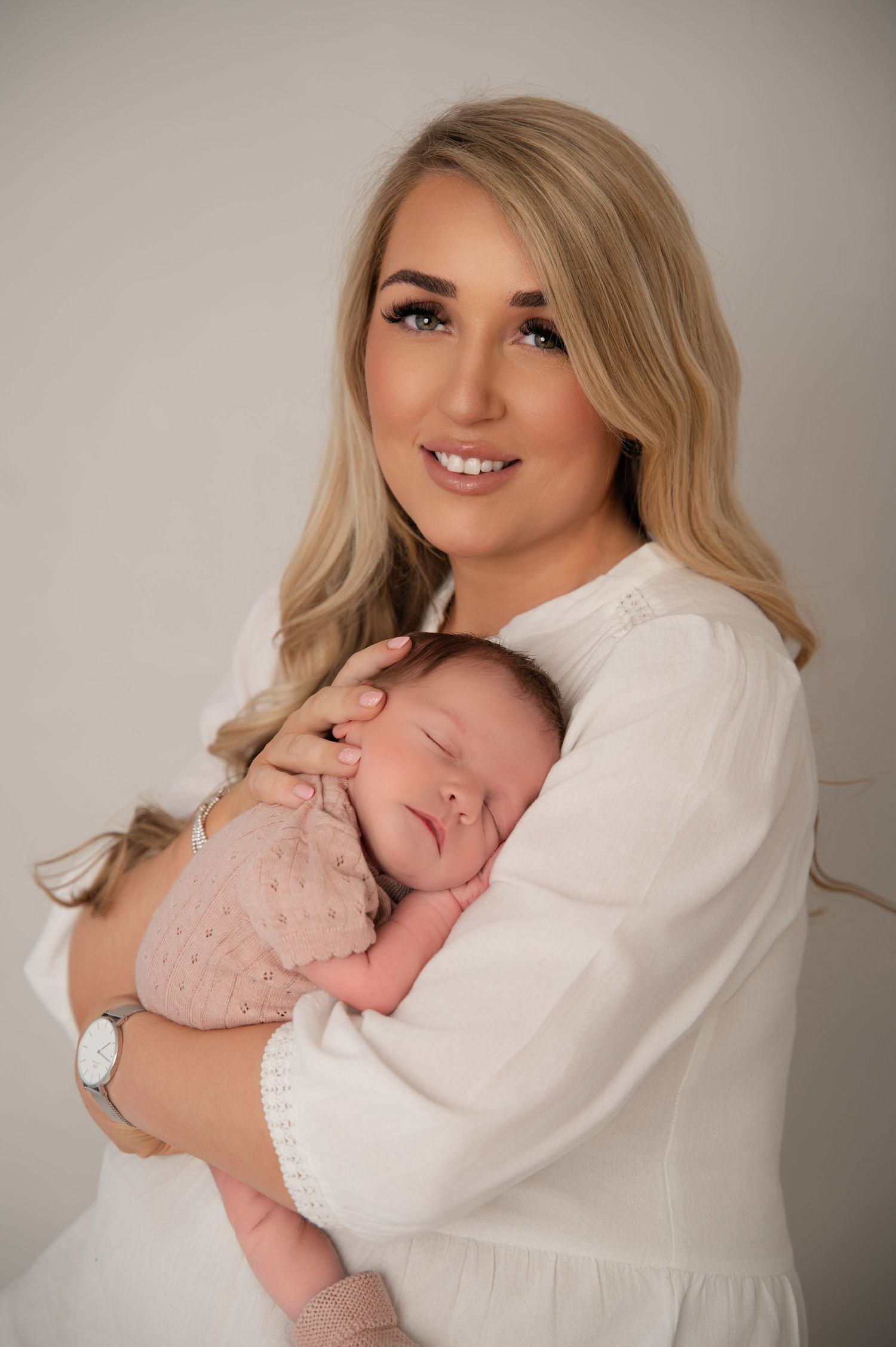 Blonde mother in white blouse cuddling her sleeping newborn baby during a soft and natural lifestyle portrait session.