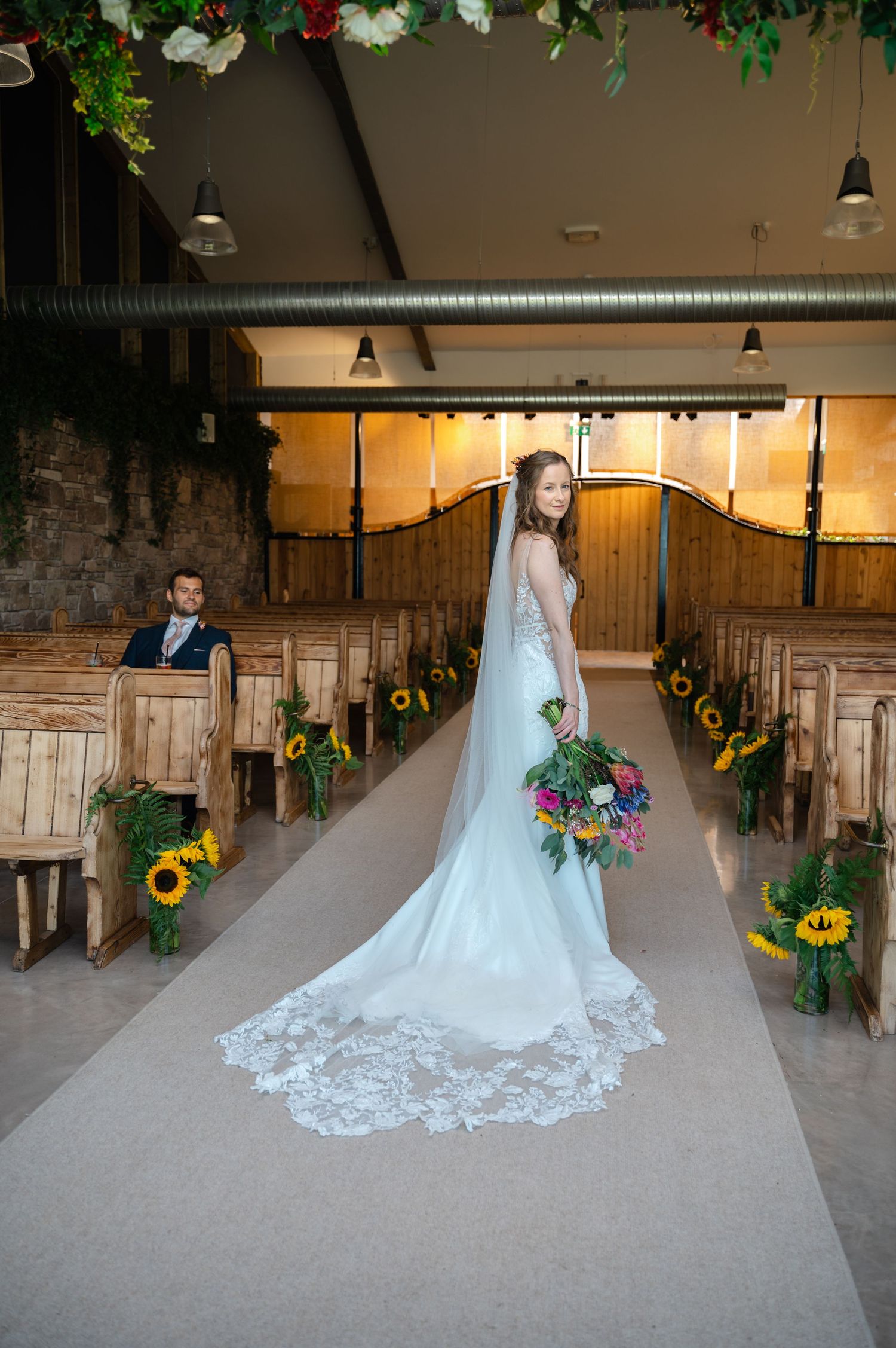 Bride walking down barn aisle with long train and floral aisle decor