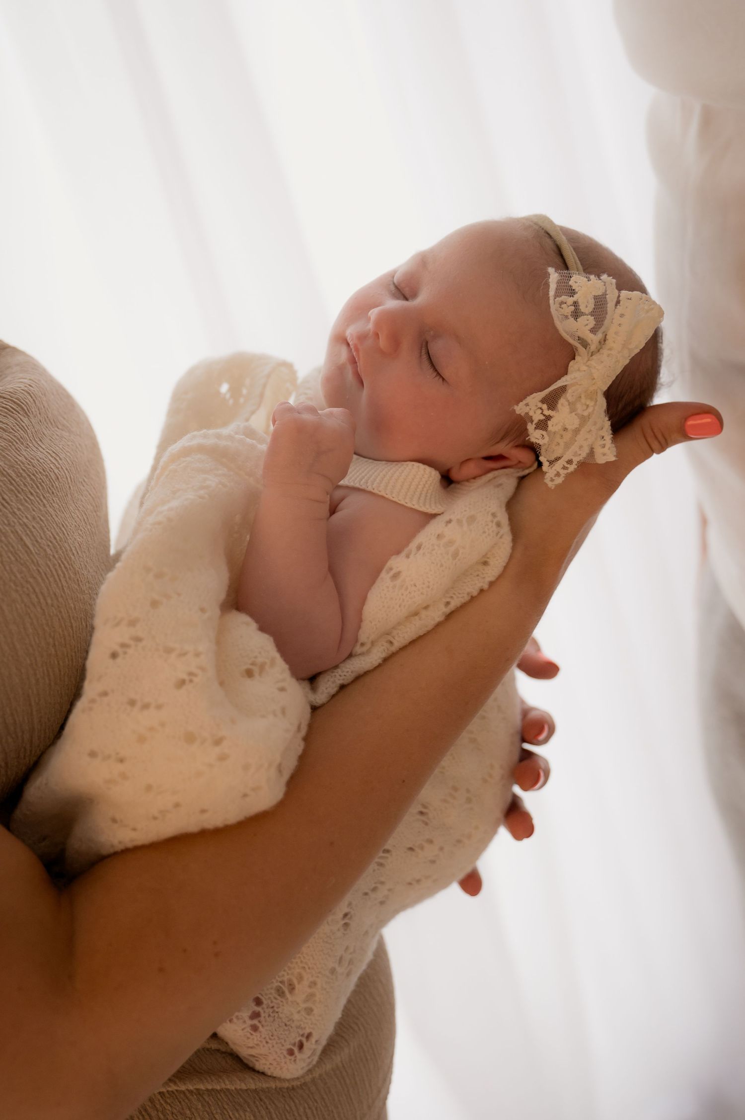 Newborn baby girl wrapped in a lace blanket and headband, cradled gently in a parent's arms during a natural light newborn session