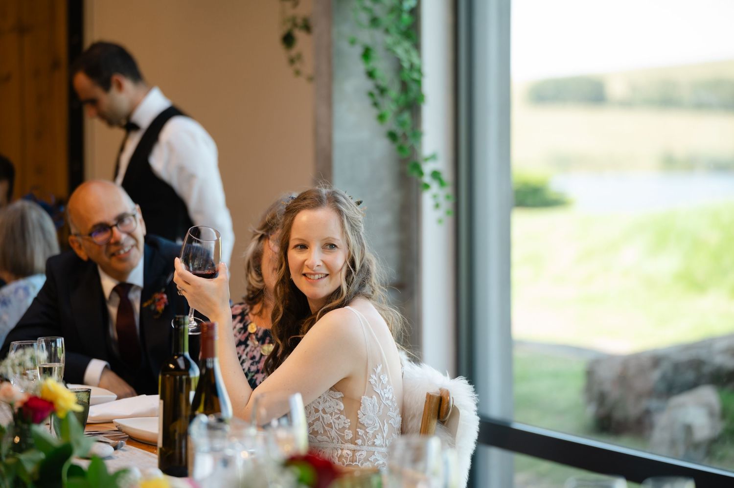 Bride smiling and raising a toast during wedding reception by the window