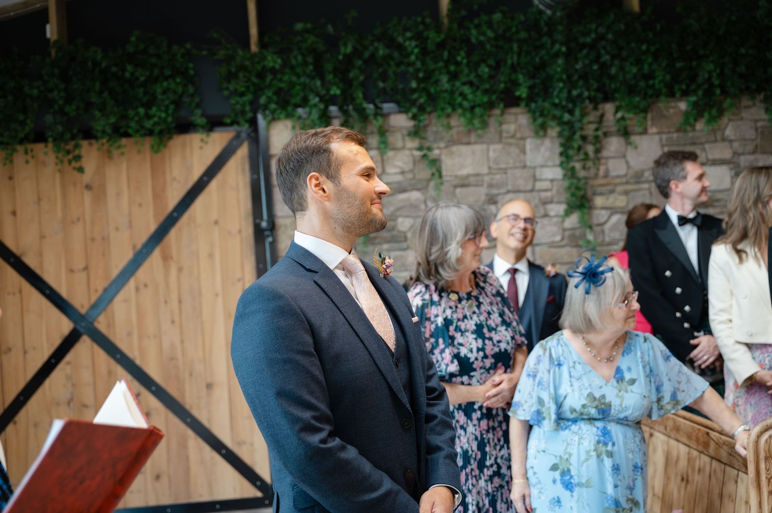 Groom standing at the altar smiling as the bride enters, with guests looking on