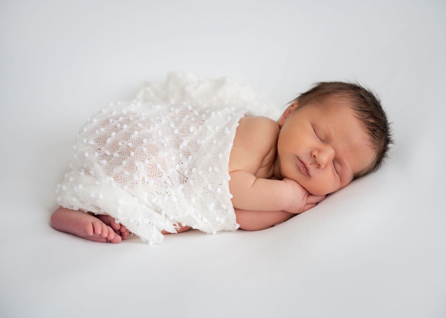 Newborn baby sleeping wrapped in a white blanket during an at-home session