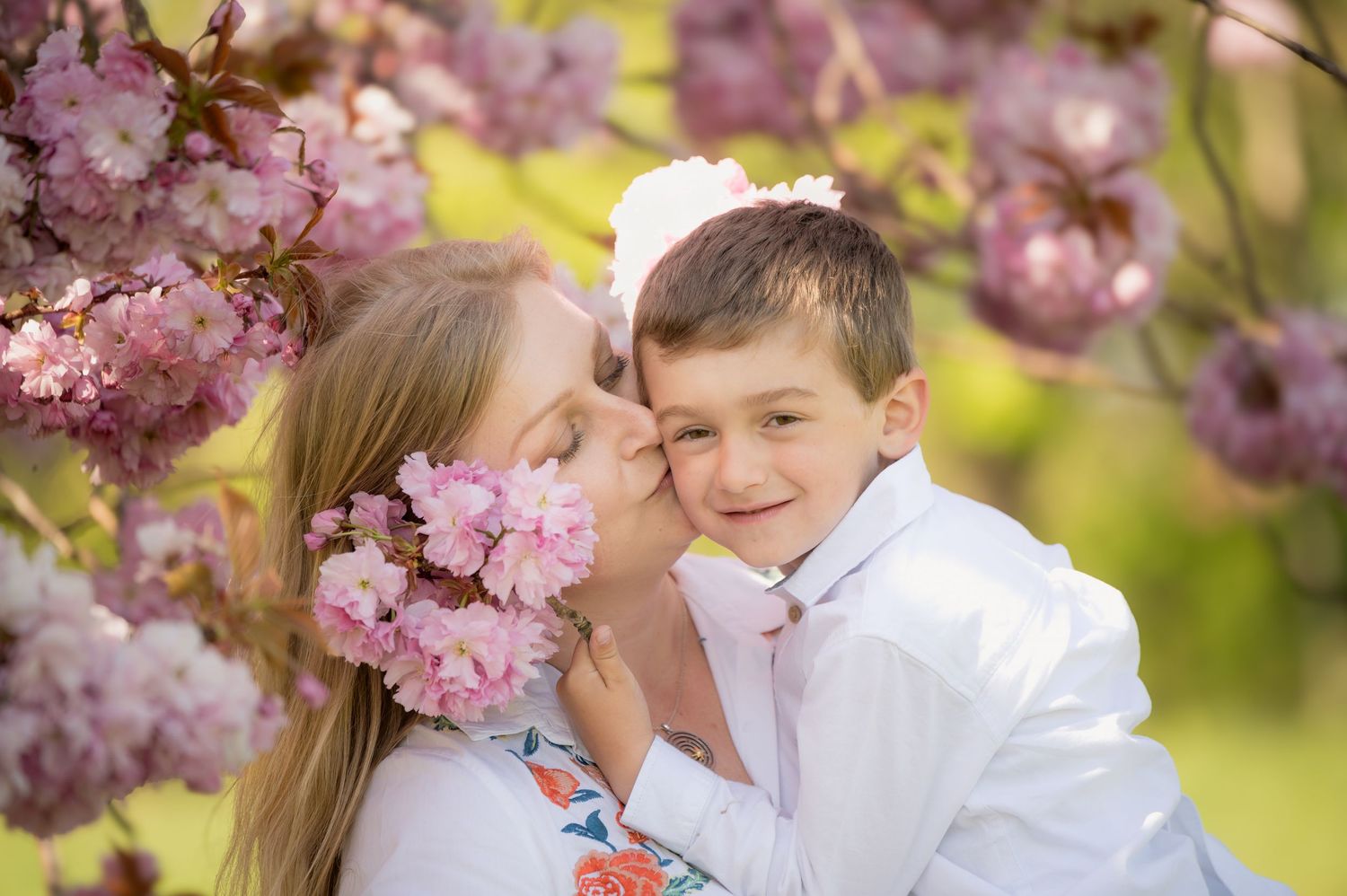 Mother and son sharing a joyful moment under blooming cherry blossoms, with soft sunlight and vibrant spring colors.