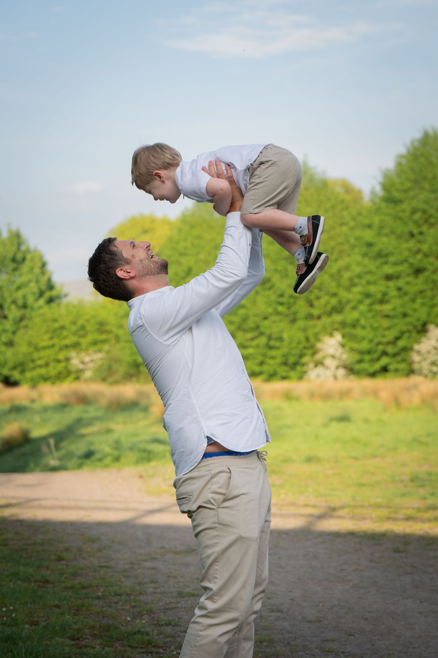 Father kneeling next to his son in a field, both holding dandelions and sharing a moment of curiosity and connection in the sunlight.