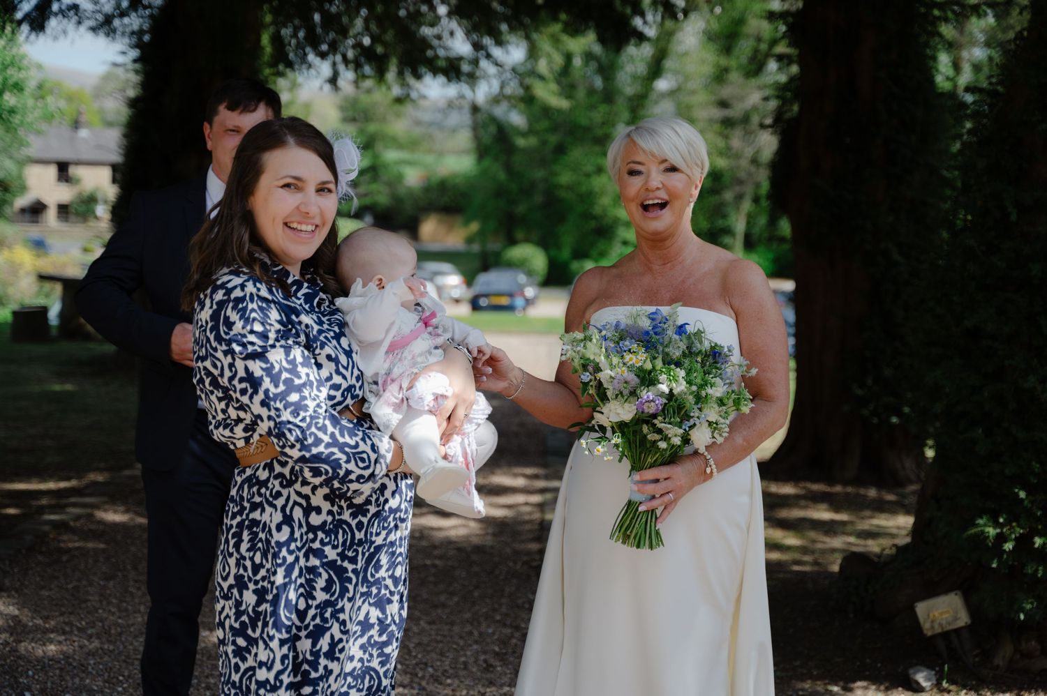 Bride holding bouquet and smiling next to a woman holding a baby.