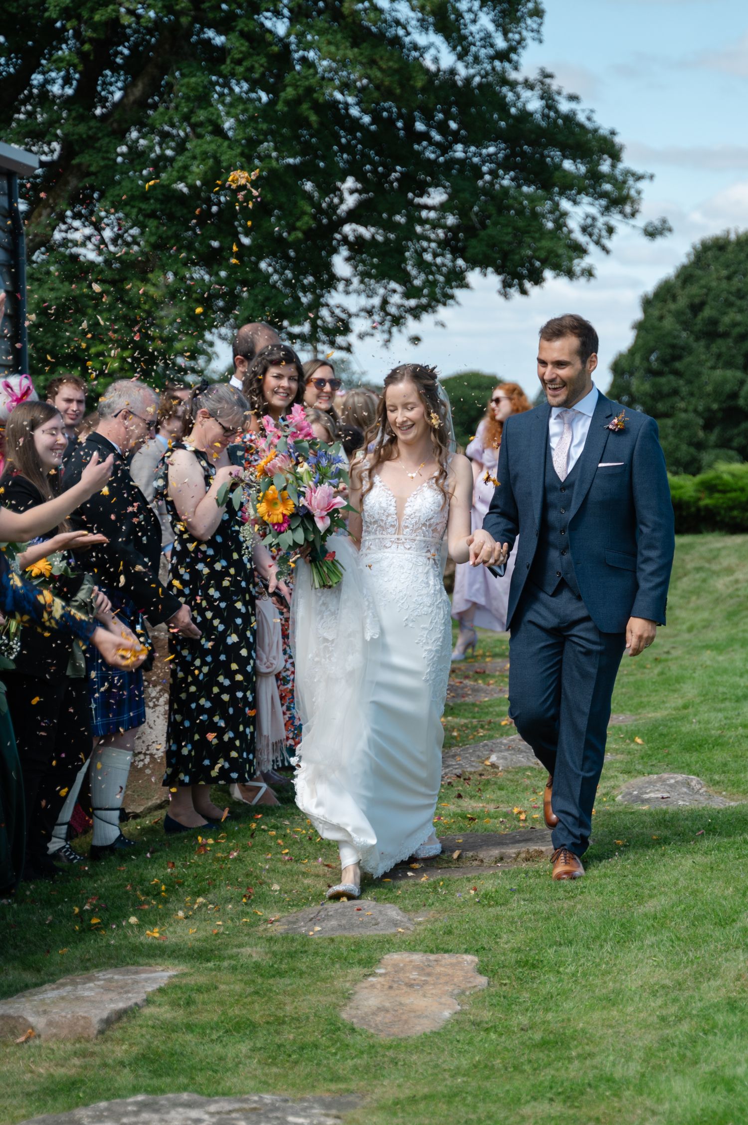 Bride and groom walking down a narrow path lined with guests throwing confetti