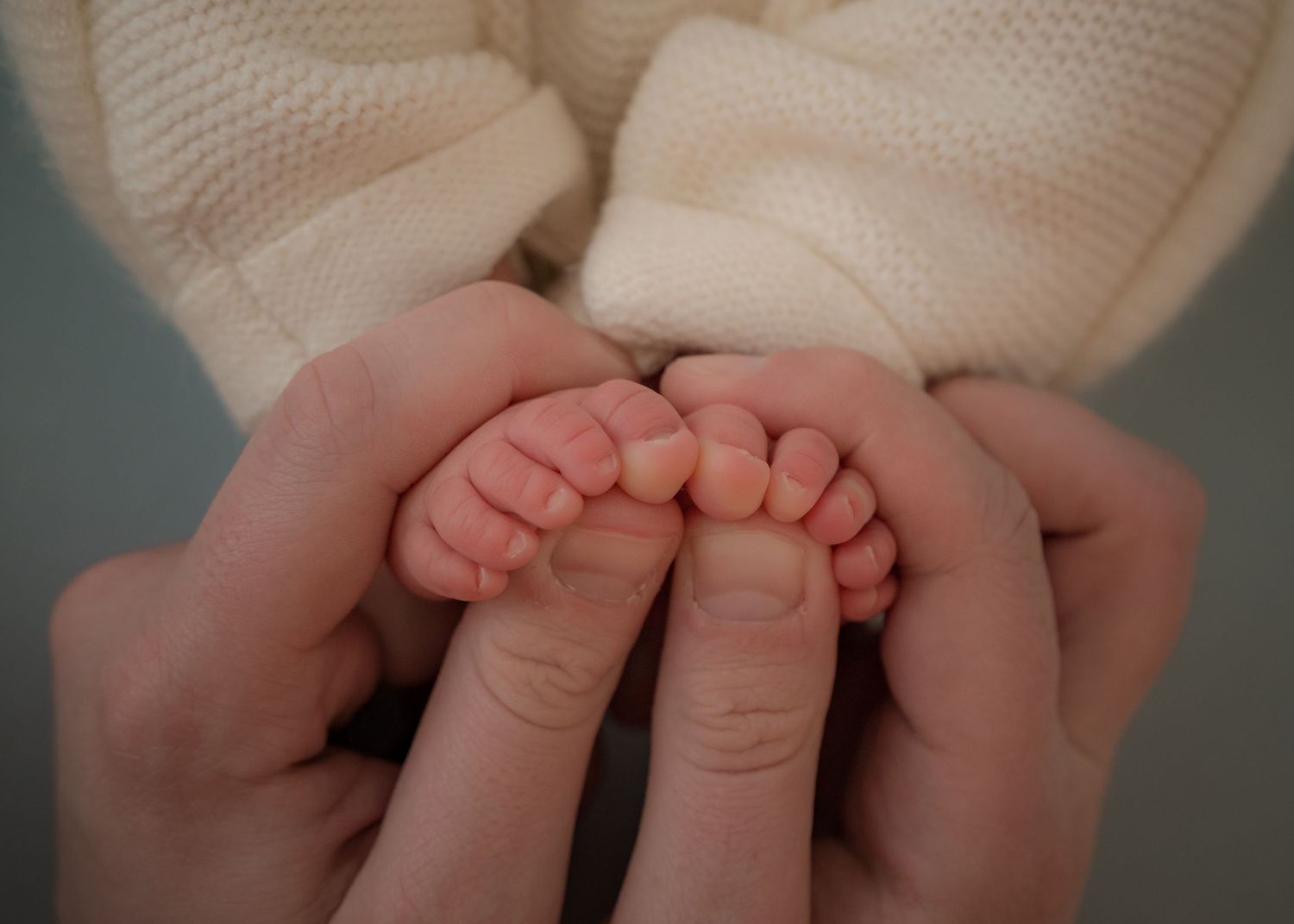 Tiny newborn feet gently held in adult hands, close-up with a soft focus, showing warmth and delicate care.
