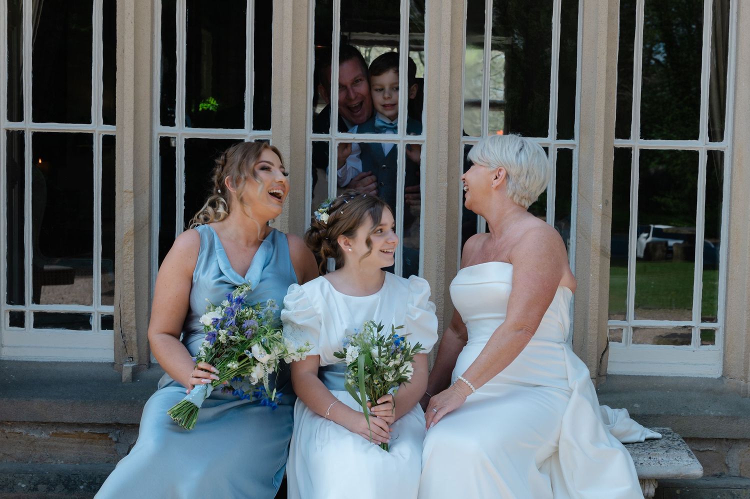 Bride laughing with bridesmaids while seated on steps holding bouquets.