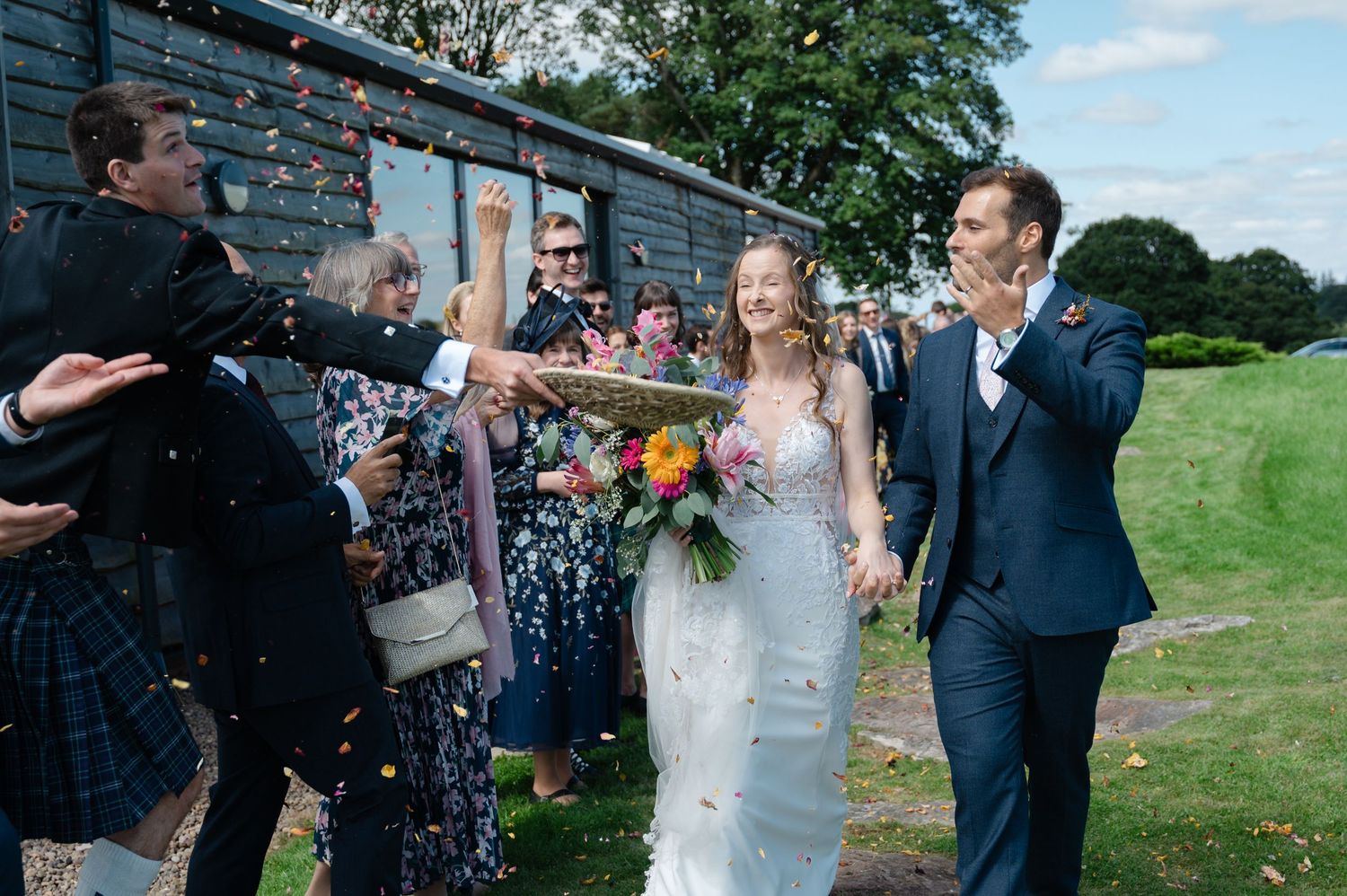 Bride and groom walking through cheering guests as confetti is tossed in the air