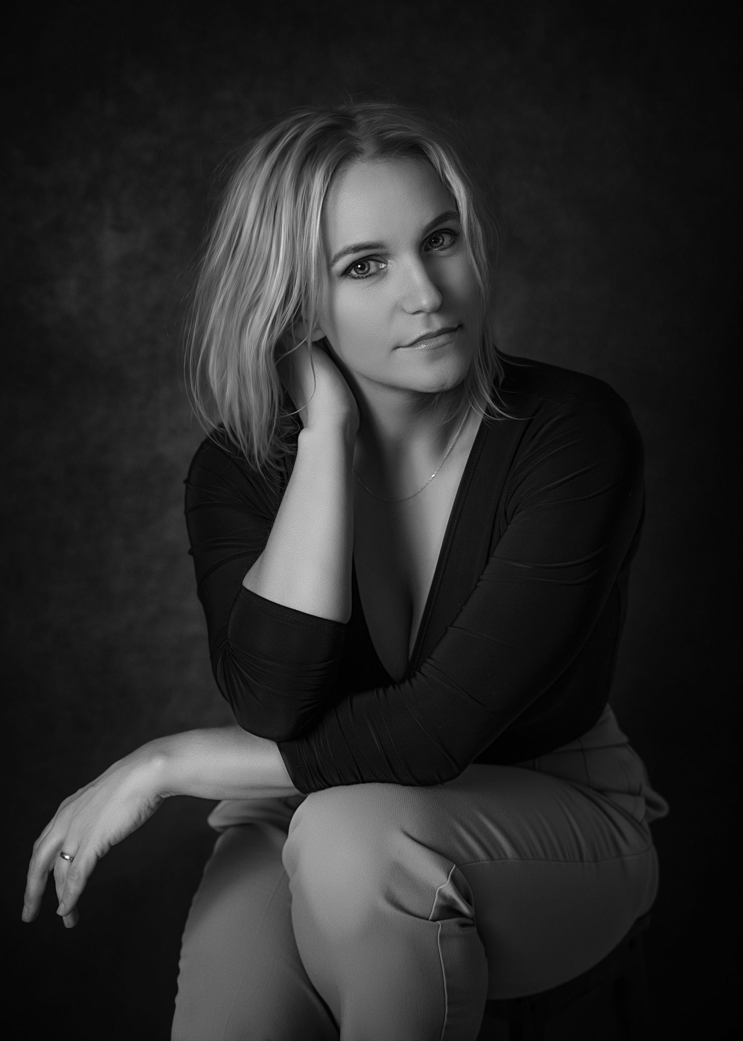 Black and white portrait of a thoughtful woman seated, with her chin resting on her hand, exuding quiet strength and elegance.