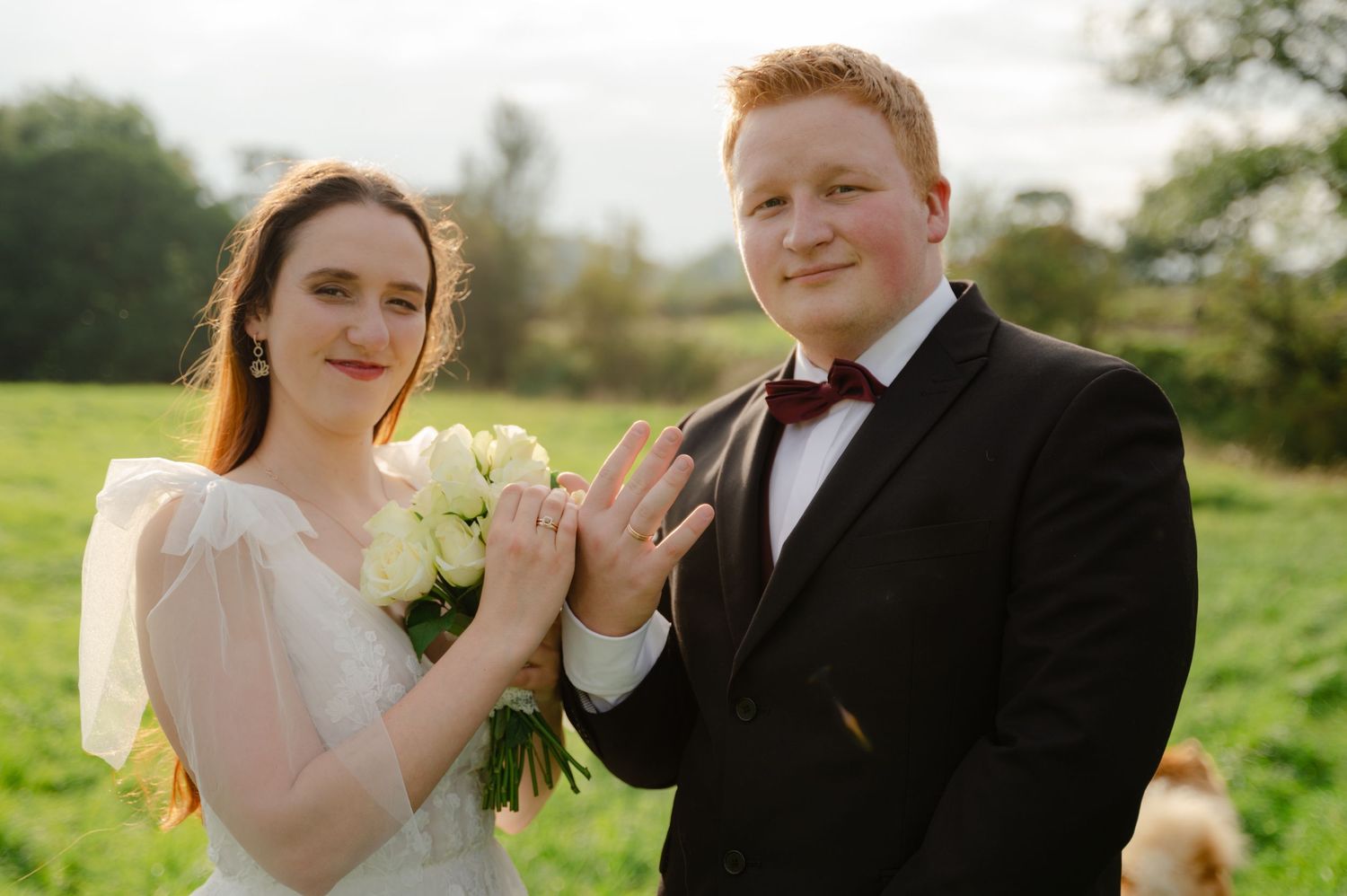 Bride and groom smiling and holding hands in a countryside setting