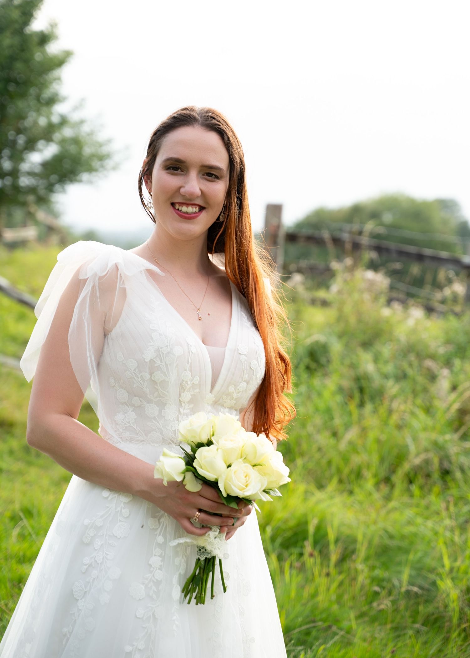 Bride smiling and holding bouquet while standing alone in a field