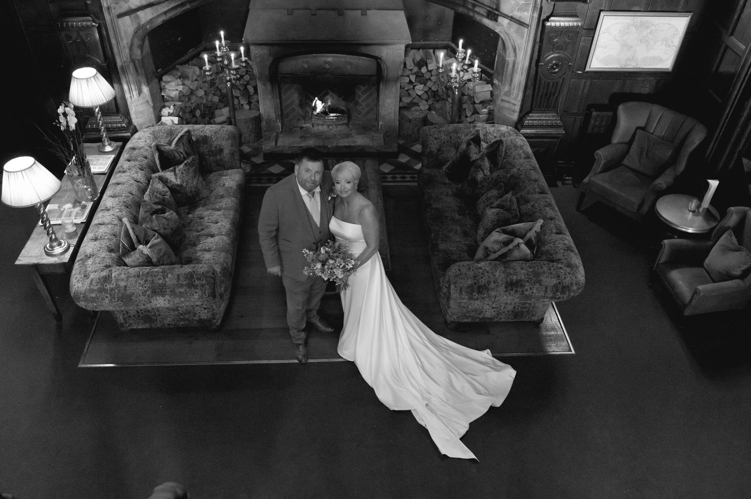 Artistic black and white photo of the bride sitting on a vintage sofa, reflected in a large mirror above, holding her bouquet.