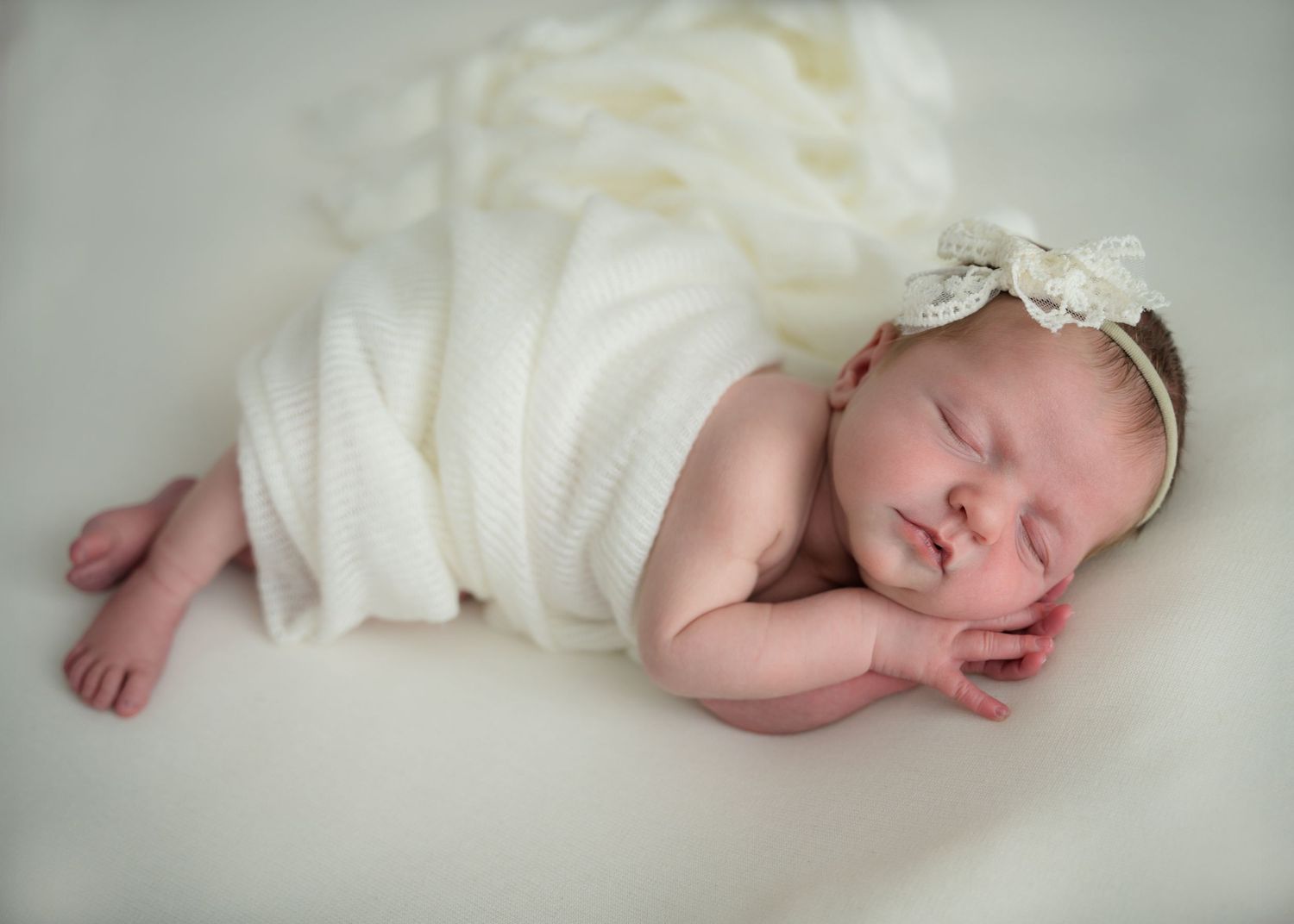 Newborn baby in white outfit sleeping on a textured blanket.