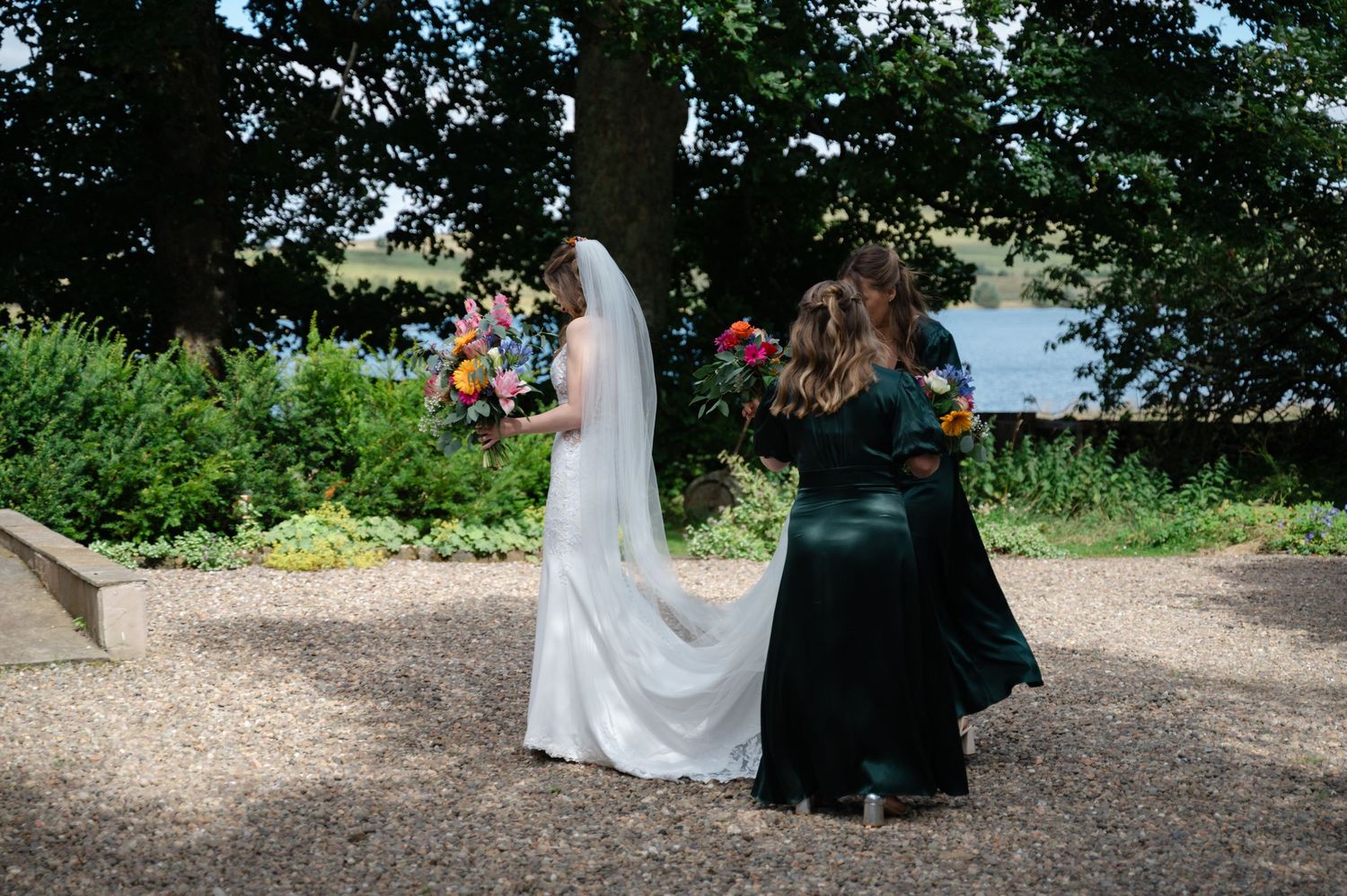 Bride warmly hugging a bridesmaid in a shaded garden spot