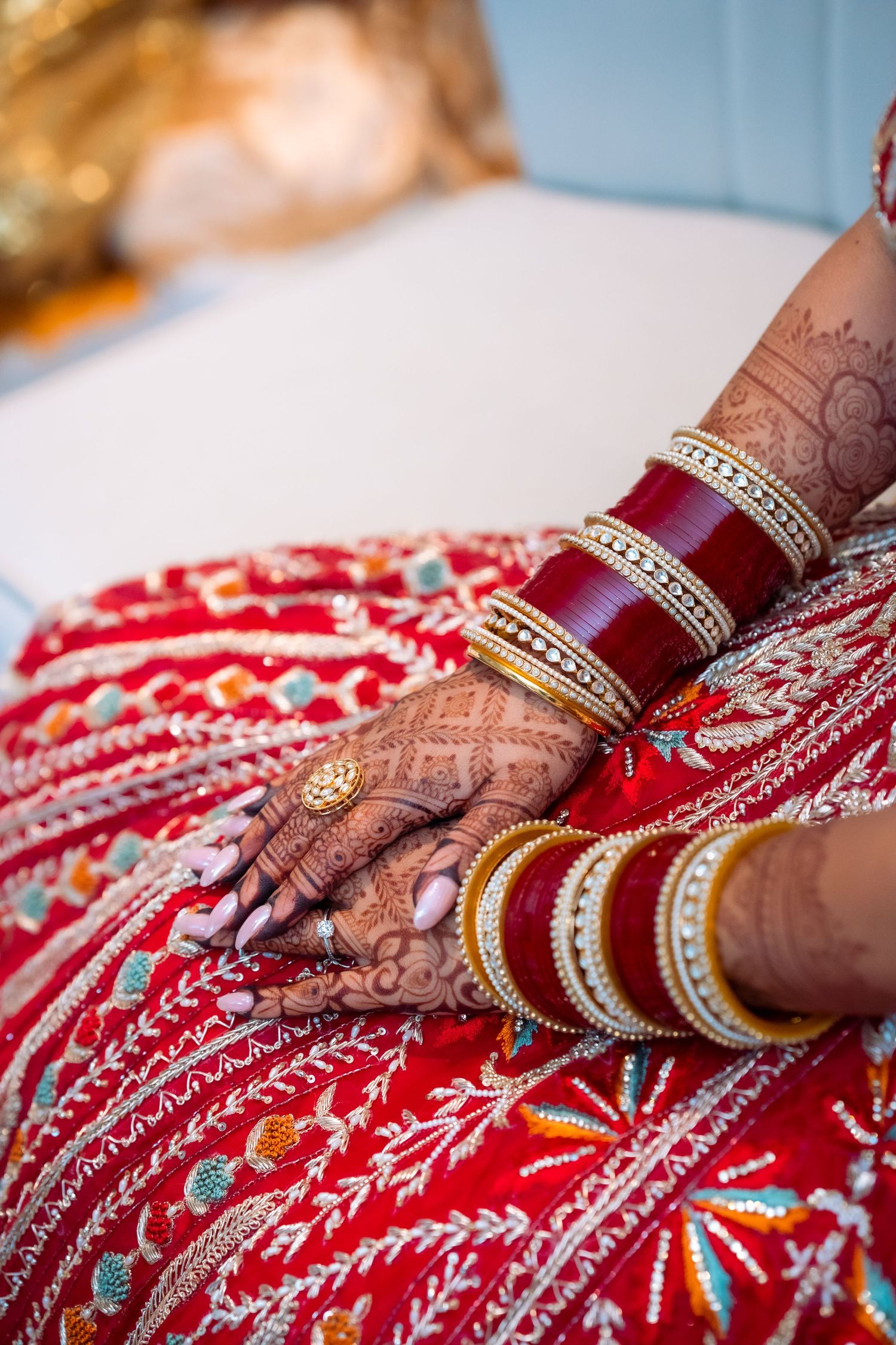 Close-up of intricate henna-decorated hands on red embroidered fabric showing traditional Indian bridal details.