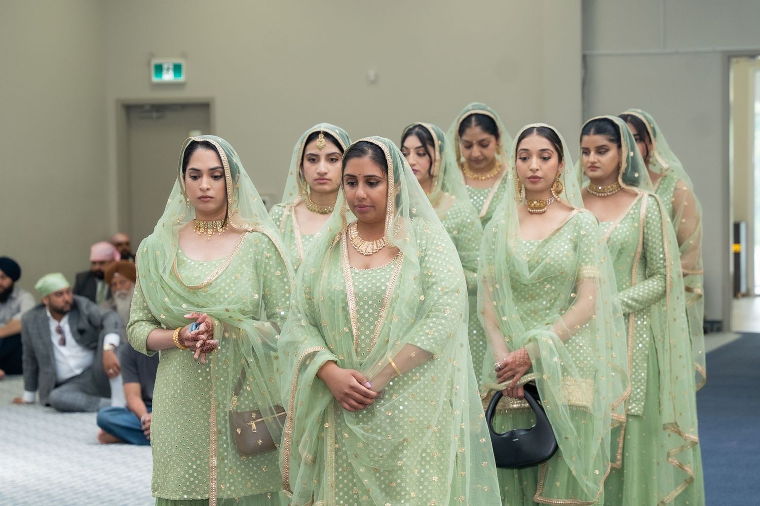 A group of people wearing matching mint green traditional outfits stand in formation during a cultural performance.