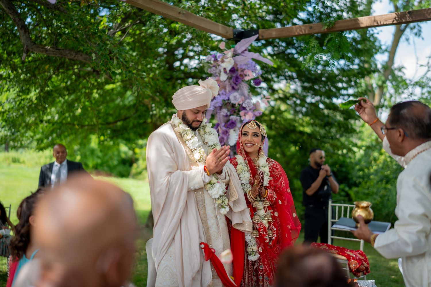 Outdoor Sikh wedding ceremony under trees with traditional white and red attire.