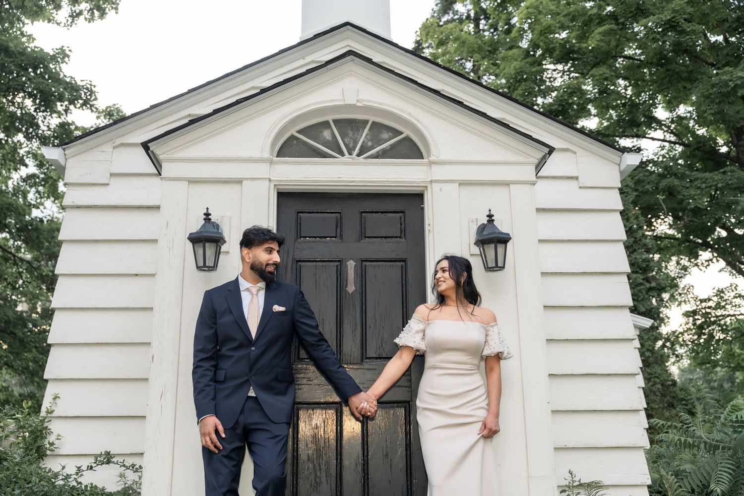 A couple shares a romantic moment outside an elegant white building with columns and lanterns.