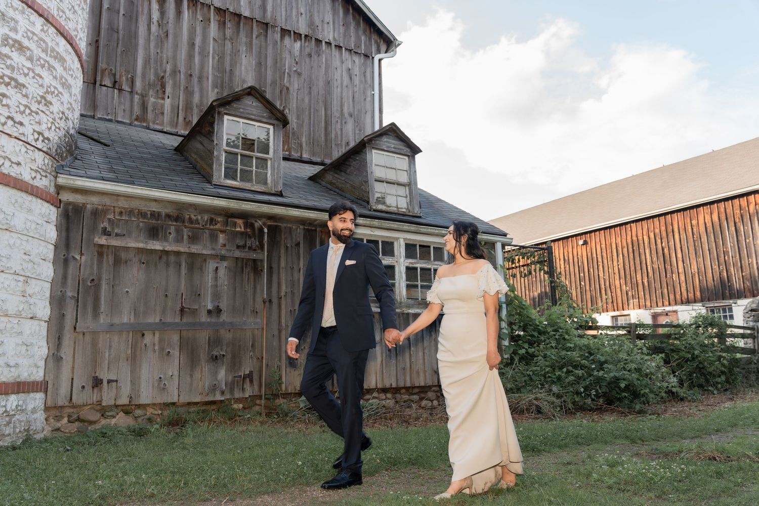 A couple stands together in front of a rustic wooden barn during a fall wedding photo session.