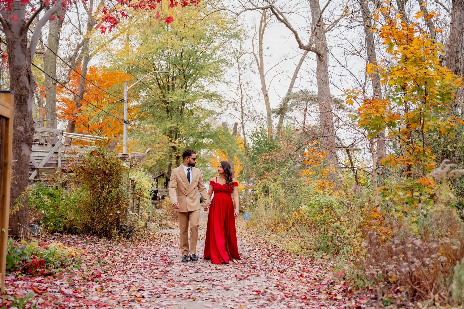 A person in a red coat walks along a leaf-covered woodland path during autumn with colorful fall foliage.