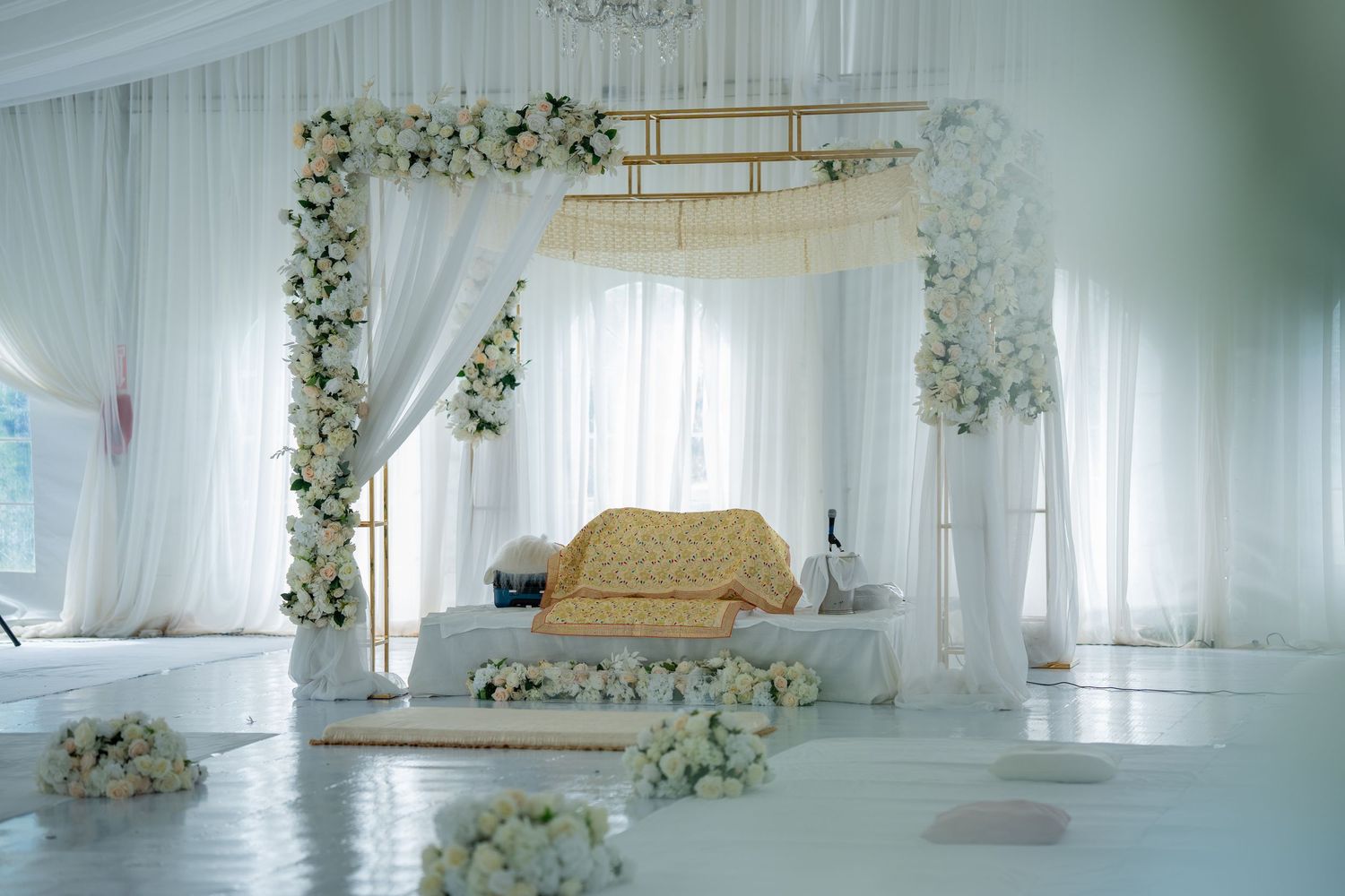 Elegant white wedding venue interior decorated with hanging floral arrangements and sheer white drapes.