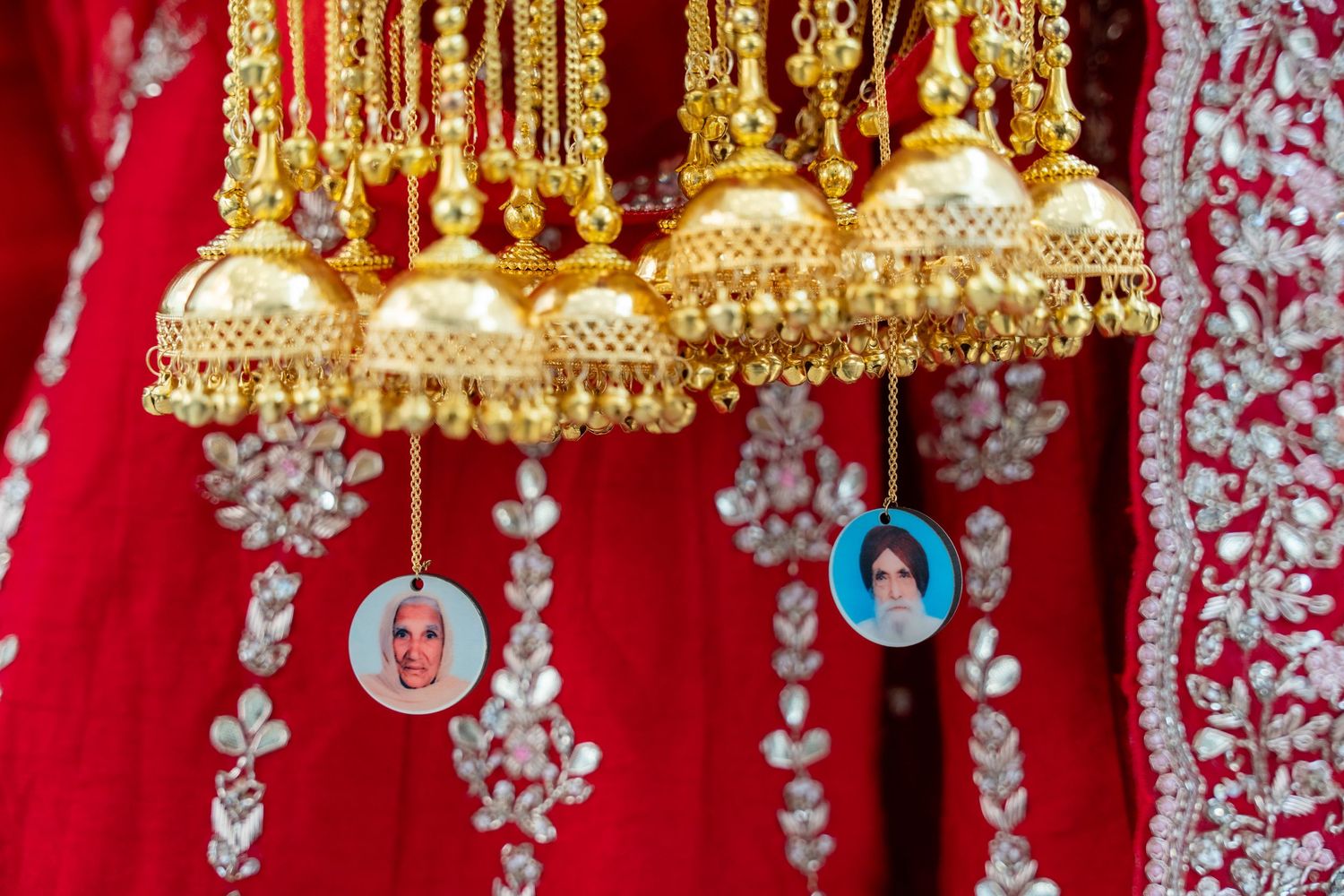 Gold traditional Indian kalire ornaments with jhumka bells and white embellishments hanging against red fabric.