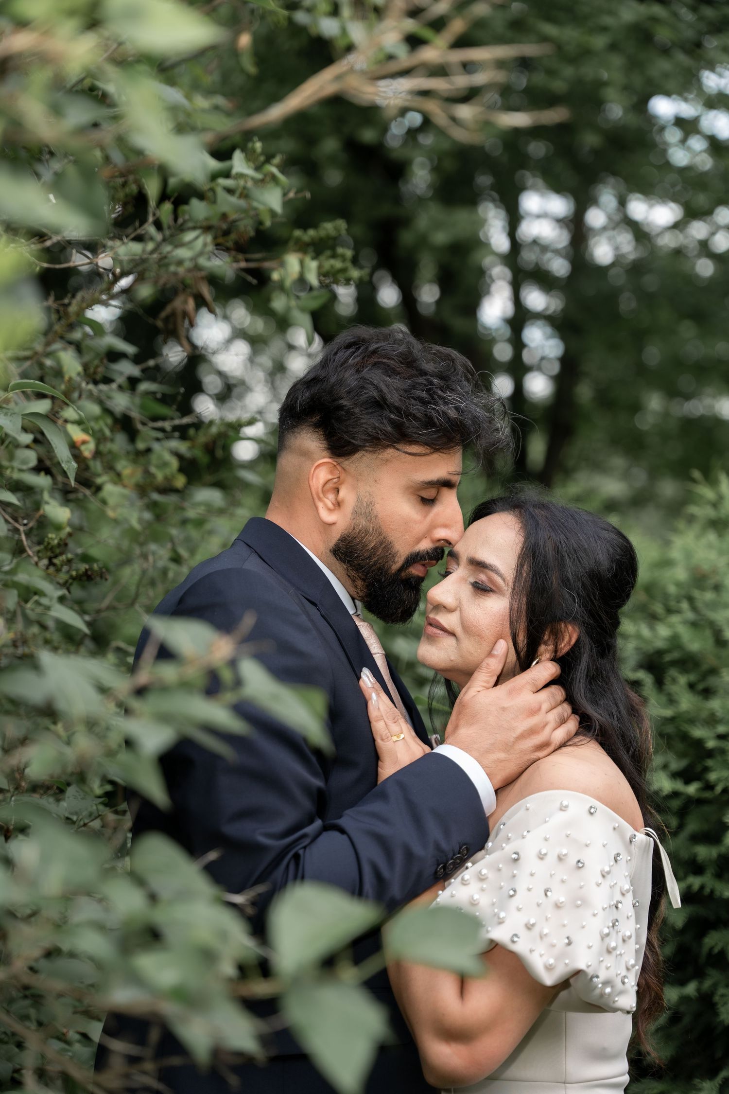 A romantic outdoor photoshoot of a couple embracing in a lush green forest setting.