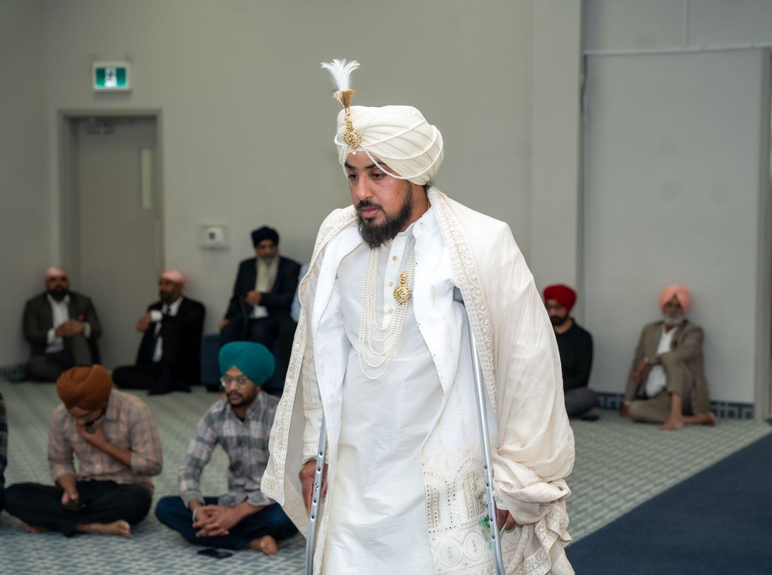 Interior view of a Sikh wedding ceremony with guests seated on floor in traditional white attire.