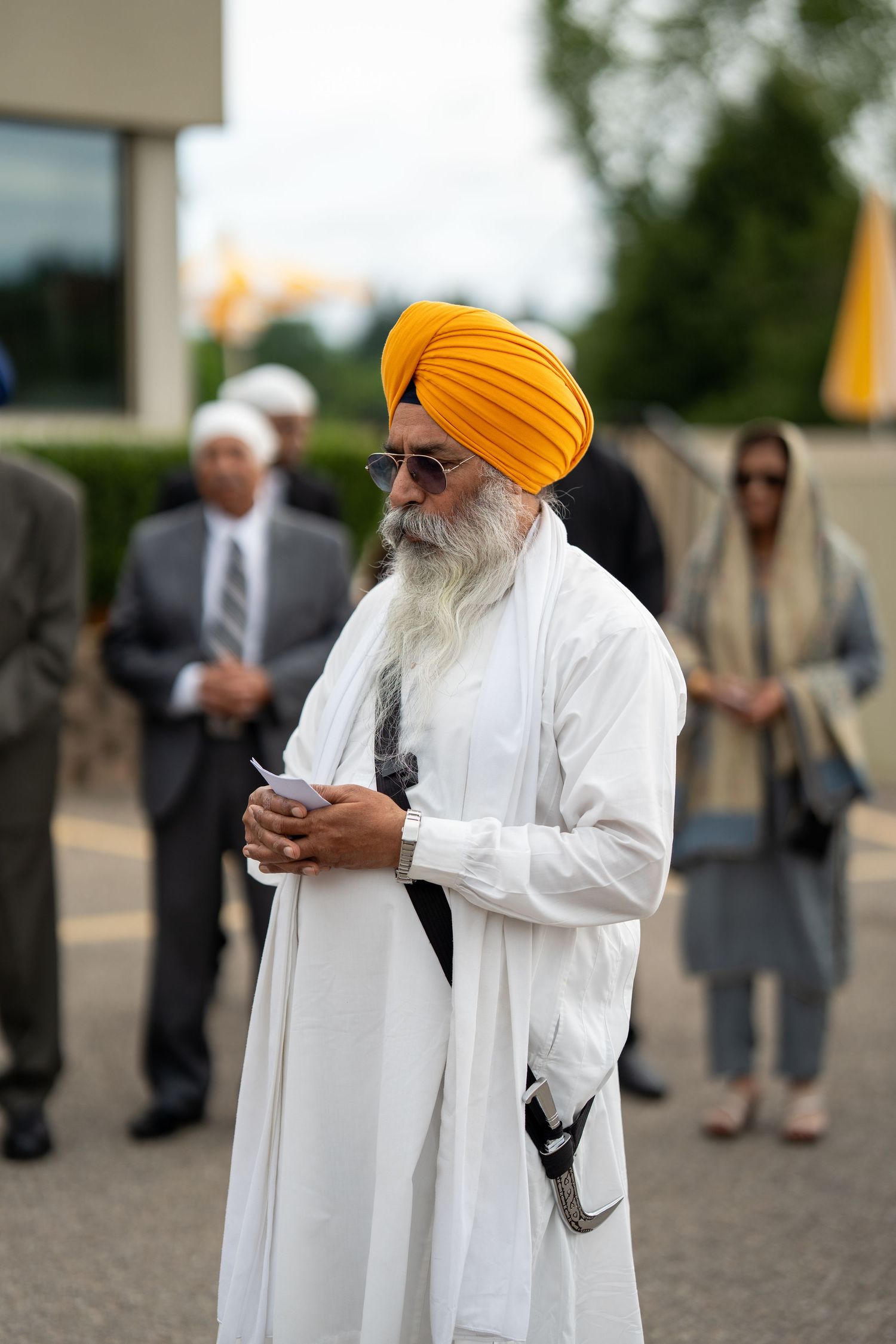 Person in white attire and orange turban checking mobile phone outdoors.
