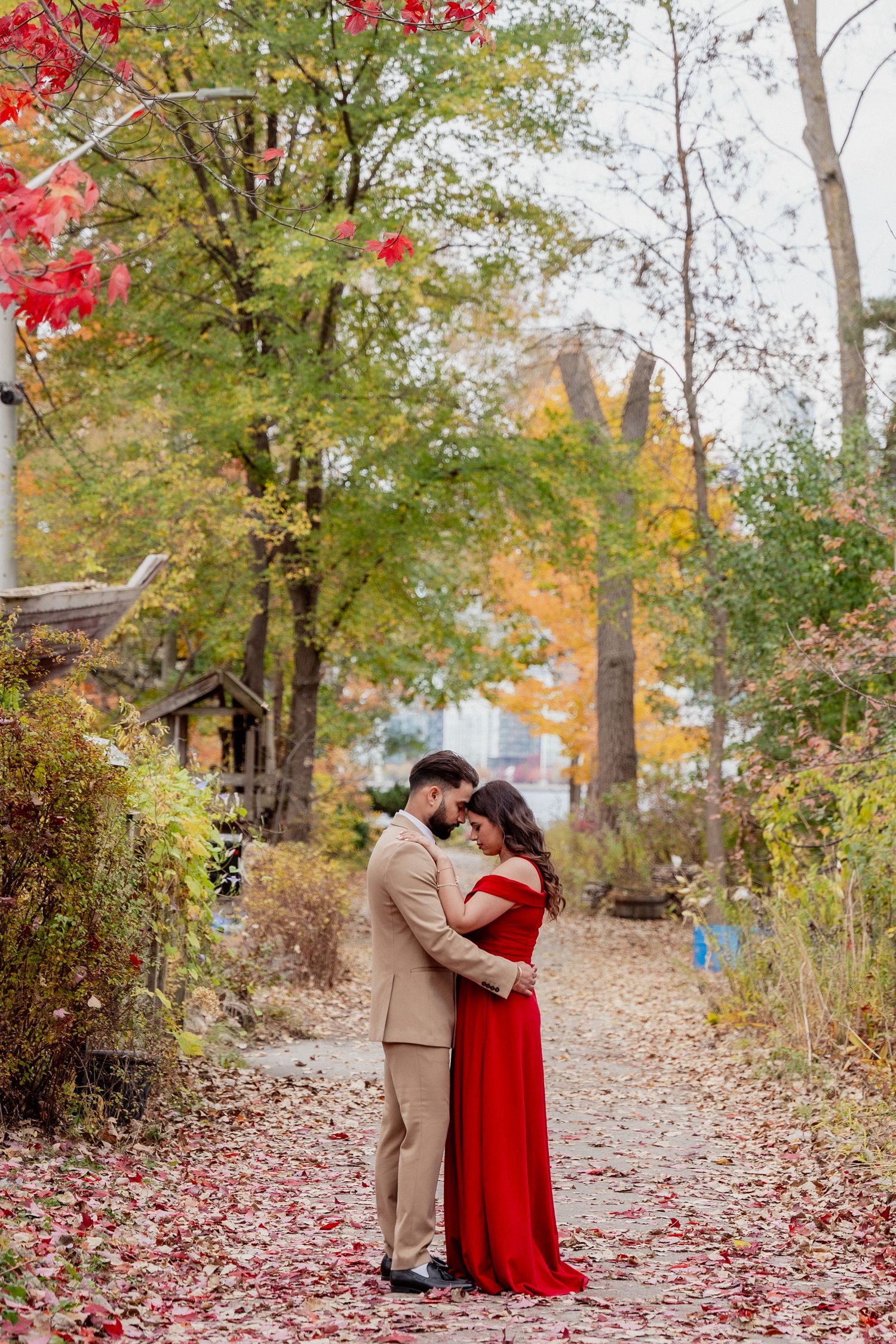A romantic autumn scene with fallen red leaves on a woodland path surrounded by trees with vibrant fall foliage.