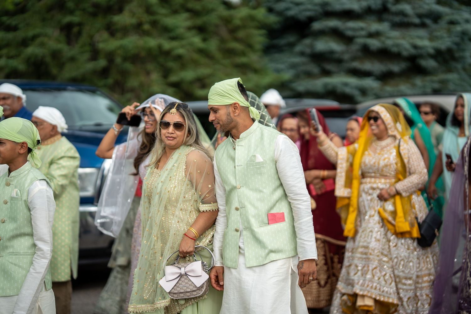 A group of people in formal attire gather outdoors for a social event on a sunny day.