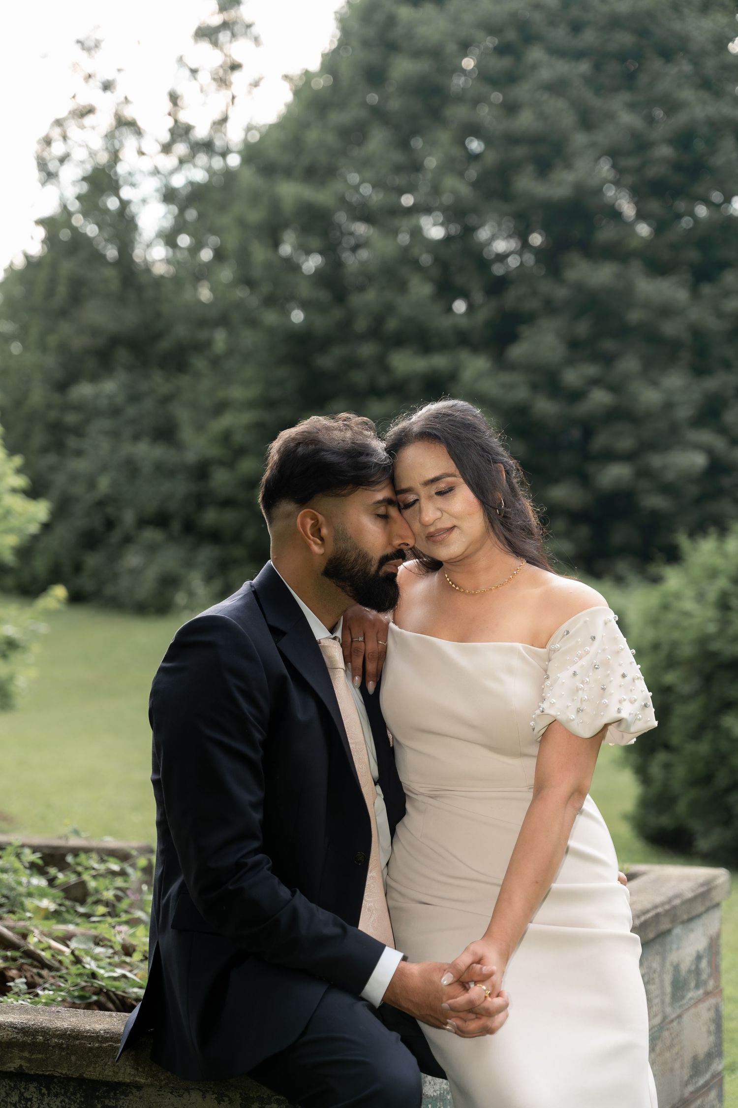 Intimate wedding couple shares tender moments while sitting together outdoors in formal attire.