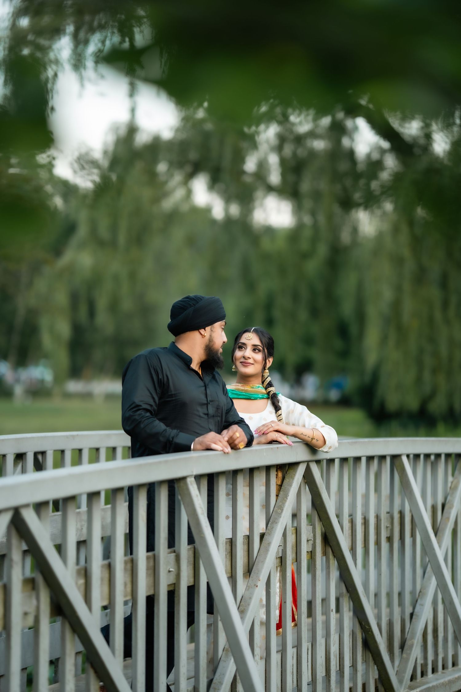 A couple shares intimate moments while posing on a wooden bridge surrounded by greenery.