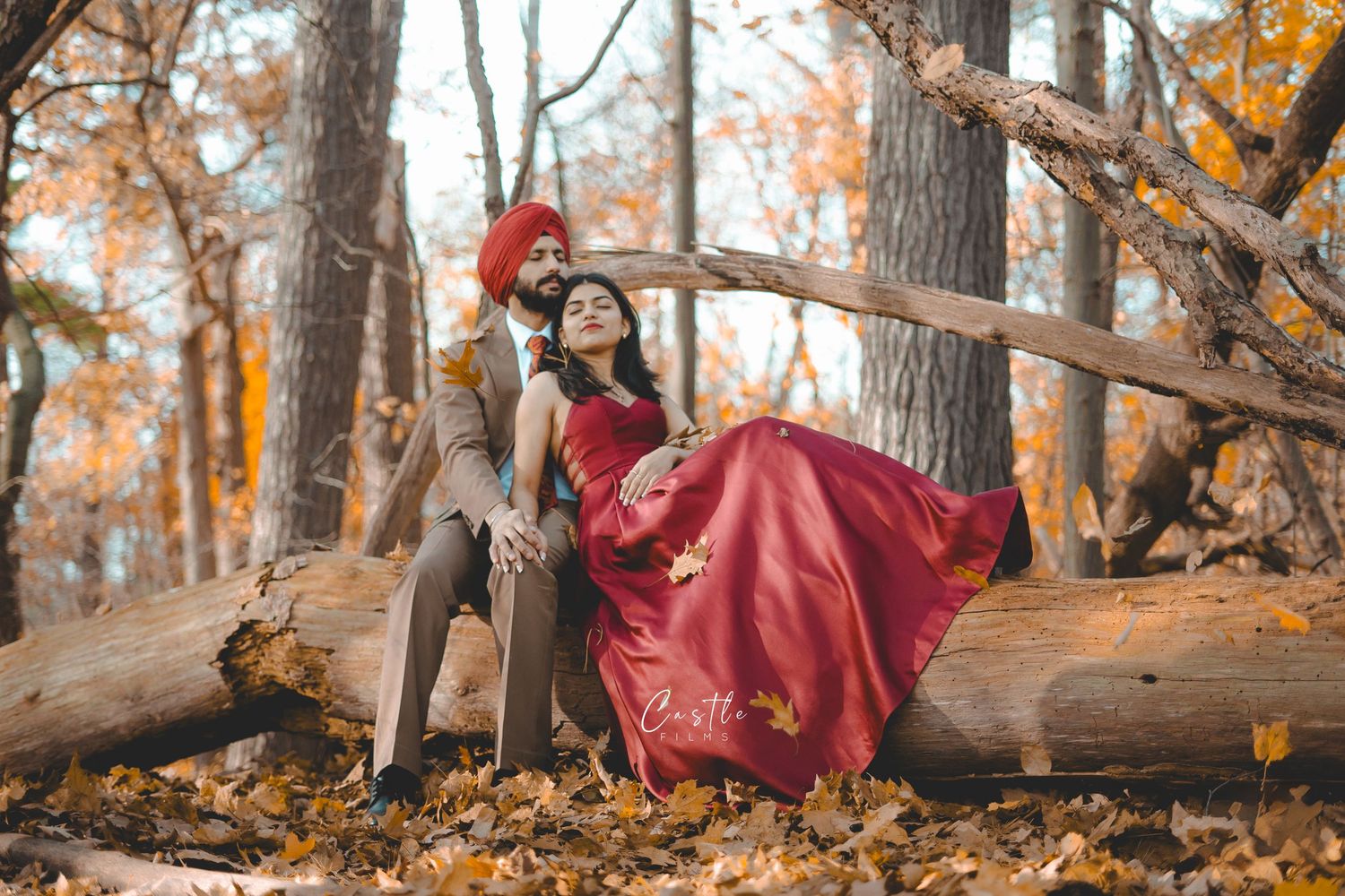 A figure in a flowing red dress poses gracefully among autumn trees and fallen leaves in a woodland setting.