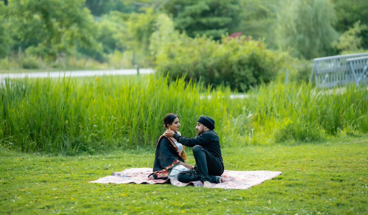Two people relax on a white blanket in a lush green meadow on a sunny summer day.