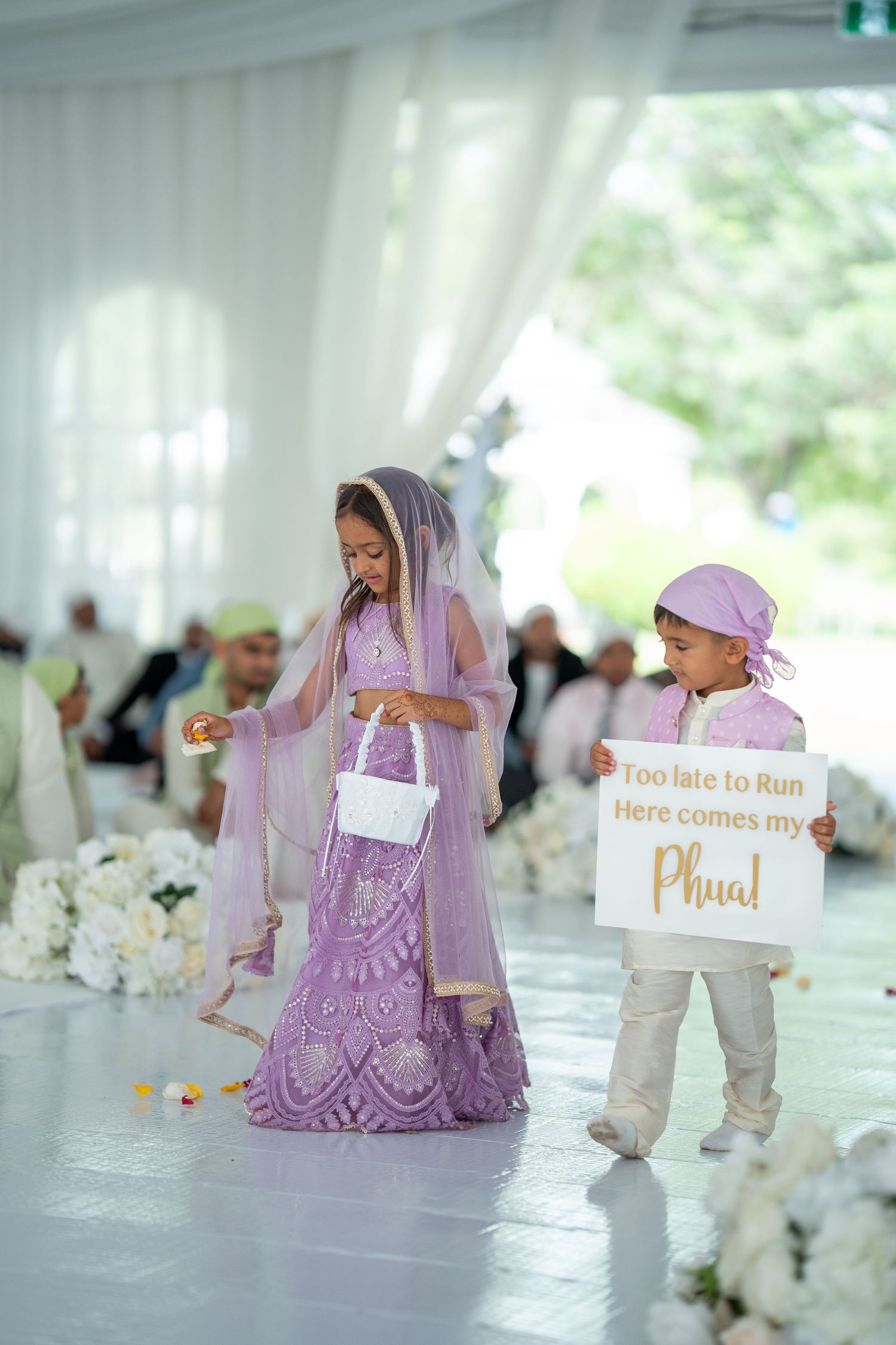 Wedding reception setup with signs and decorations in purple and white under an elegant tent.