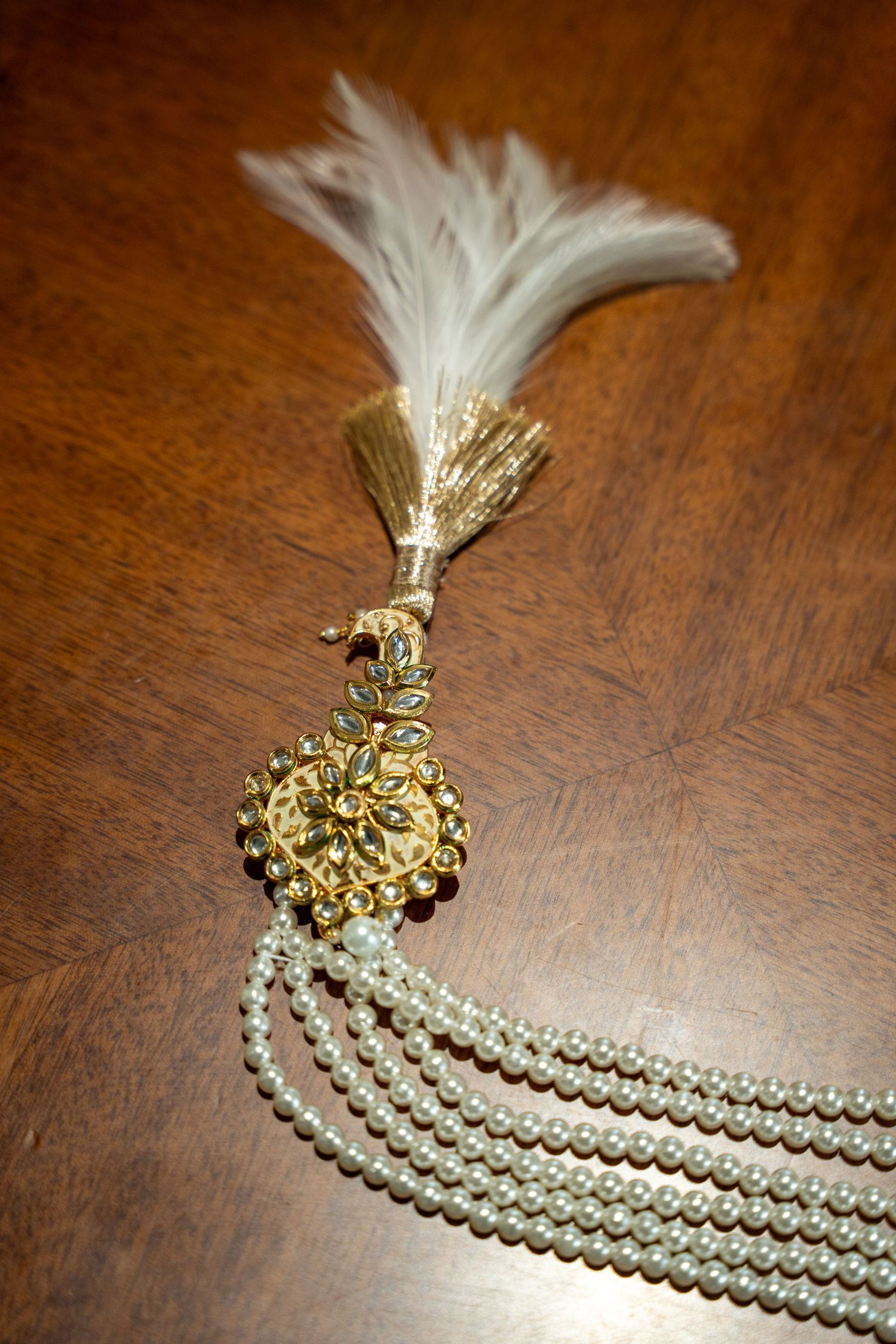 Elegant pearl necklace with gold accents and white tassel detail laid out on wooden surface.