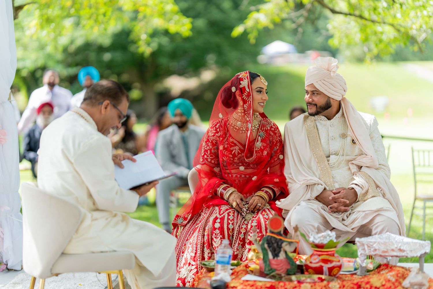 Wedding guests sit at decorated outdoor tables during a traditional South Asian celebration in a garden setting.