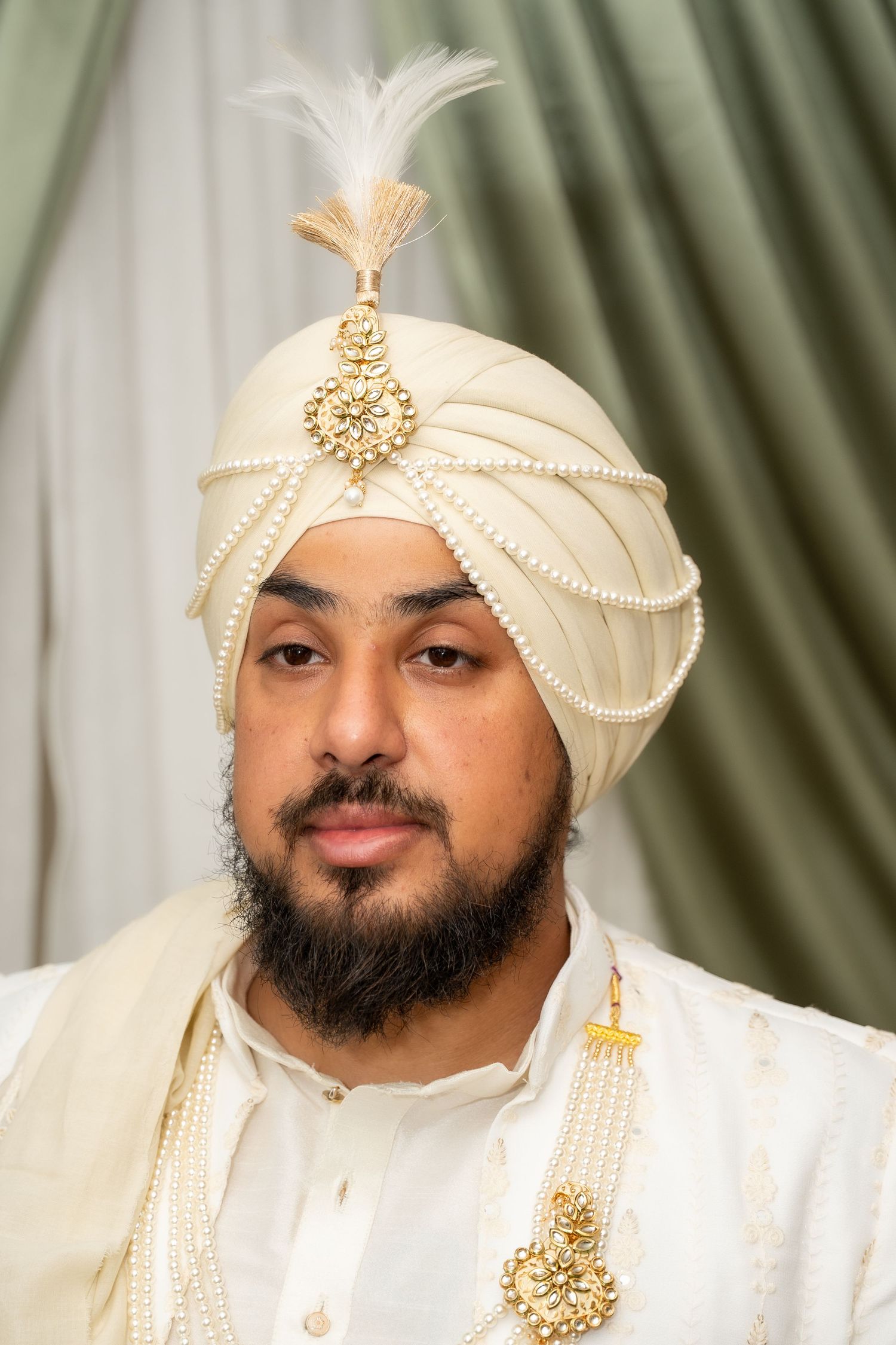 Traditional Sikh groom wearing cream turban and formal attire with ornate gold accessories.