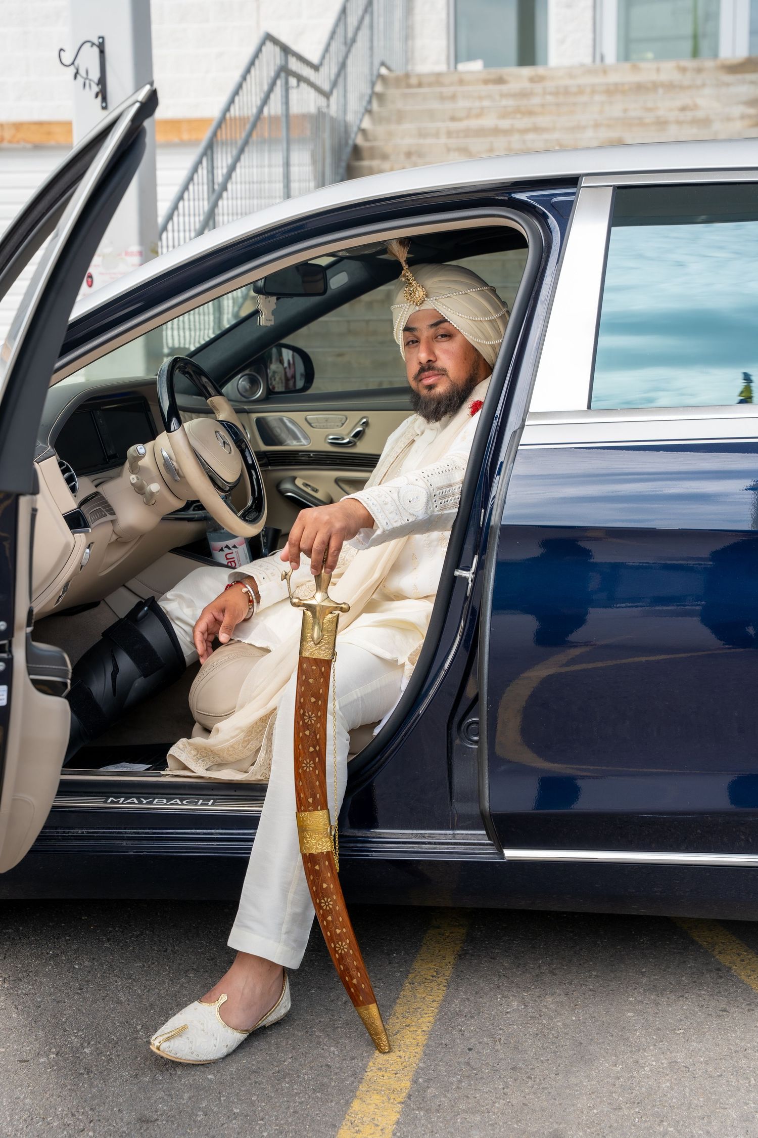 Person in white clothing getting into a dark blue luxury car.