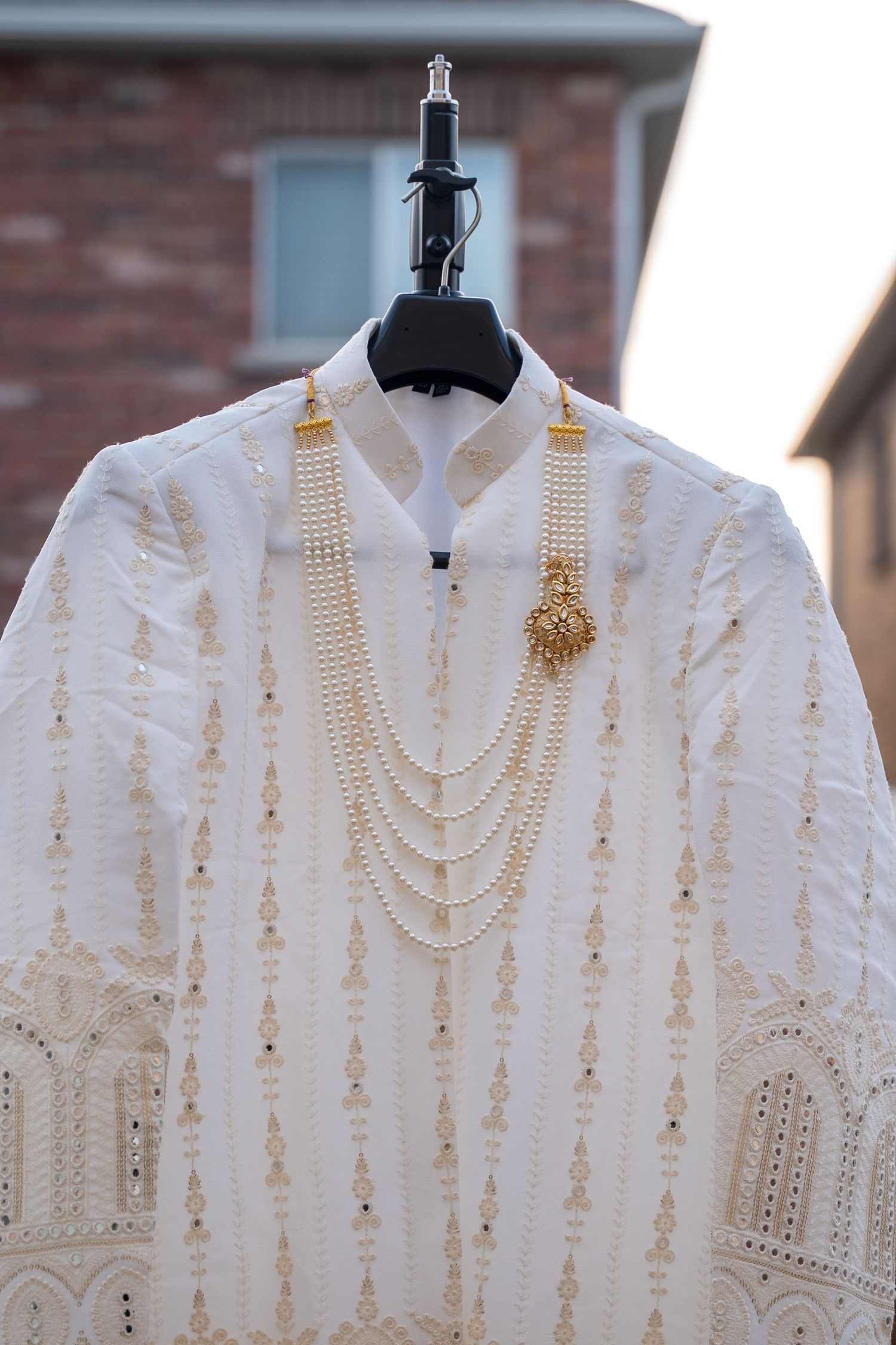 Three white lace blouses with delicate embroidery and pearl necklaces displayed on black hangers against a brick wall.