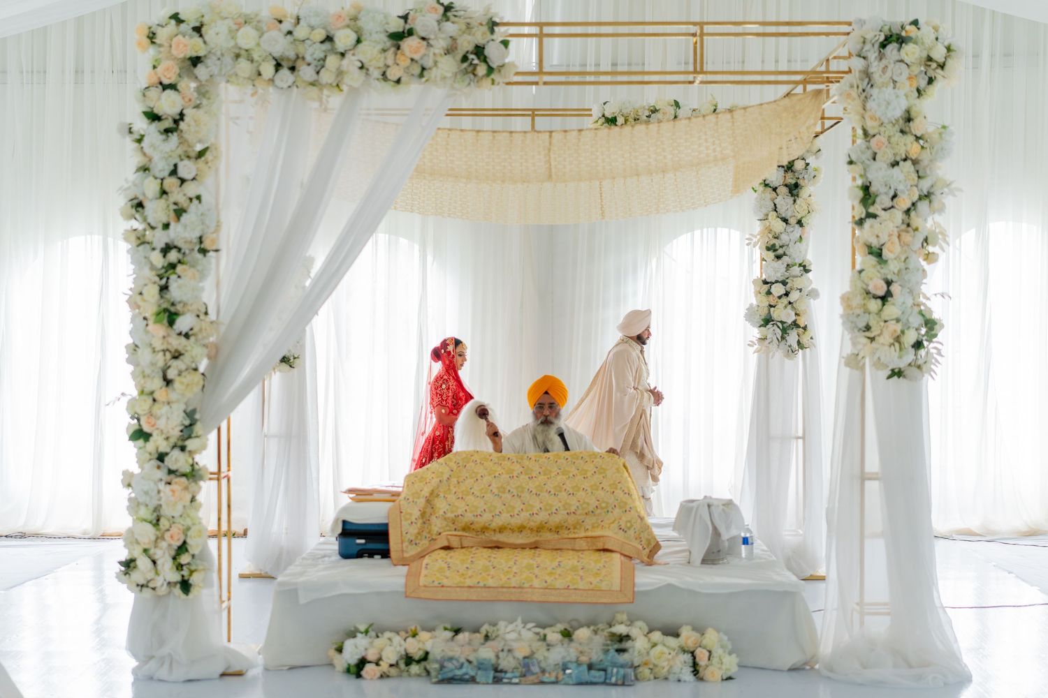 Elegant wedding venue setup with white drapes, floral arches, and golden furniture creating a romantic atmosphere.