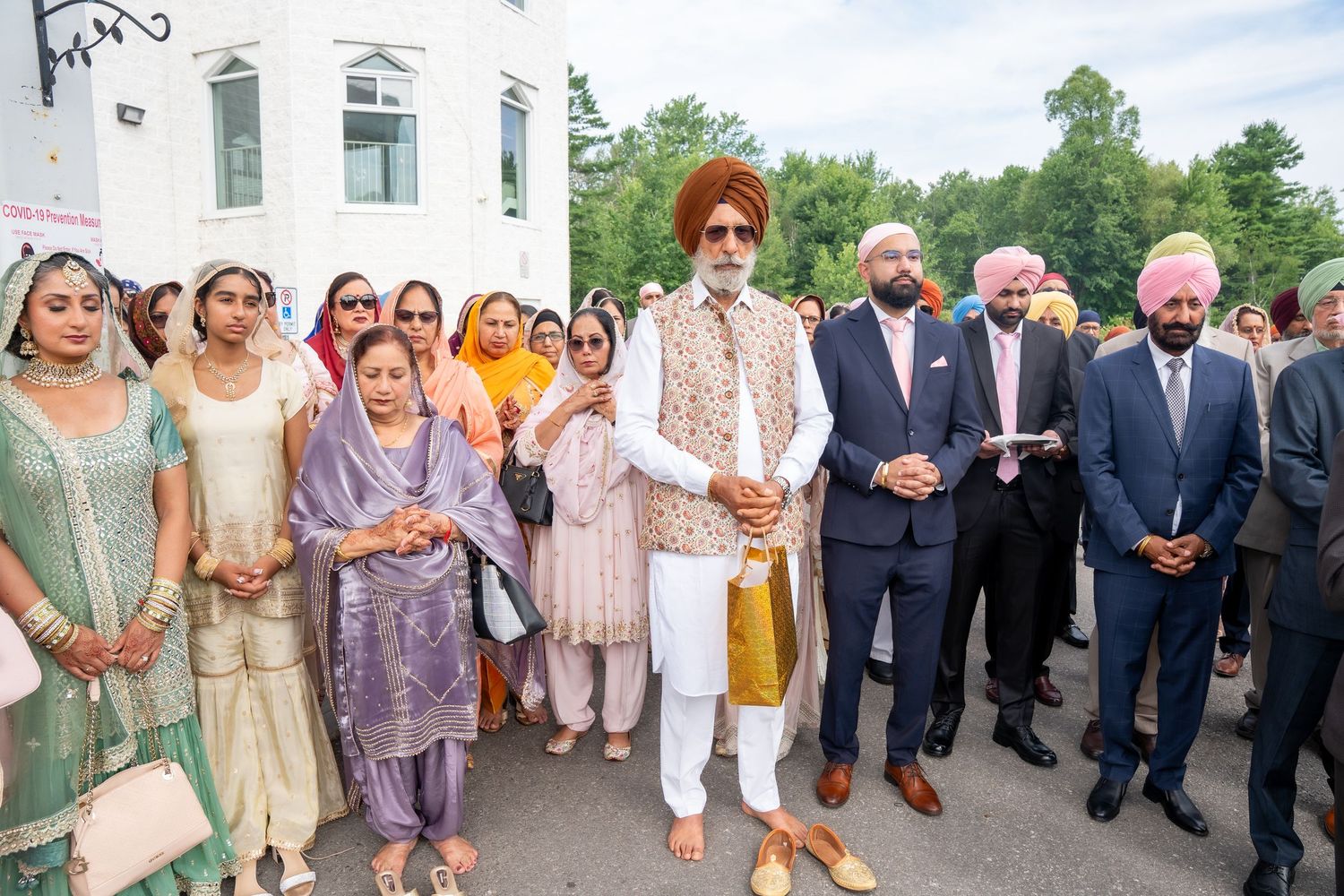 Group photo of wedding guests in traditional Indian and Western attire standing outdoors.