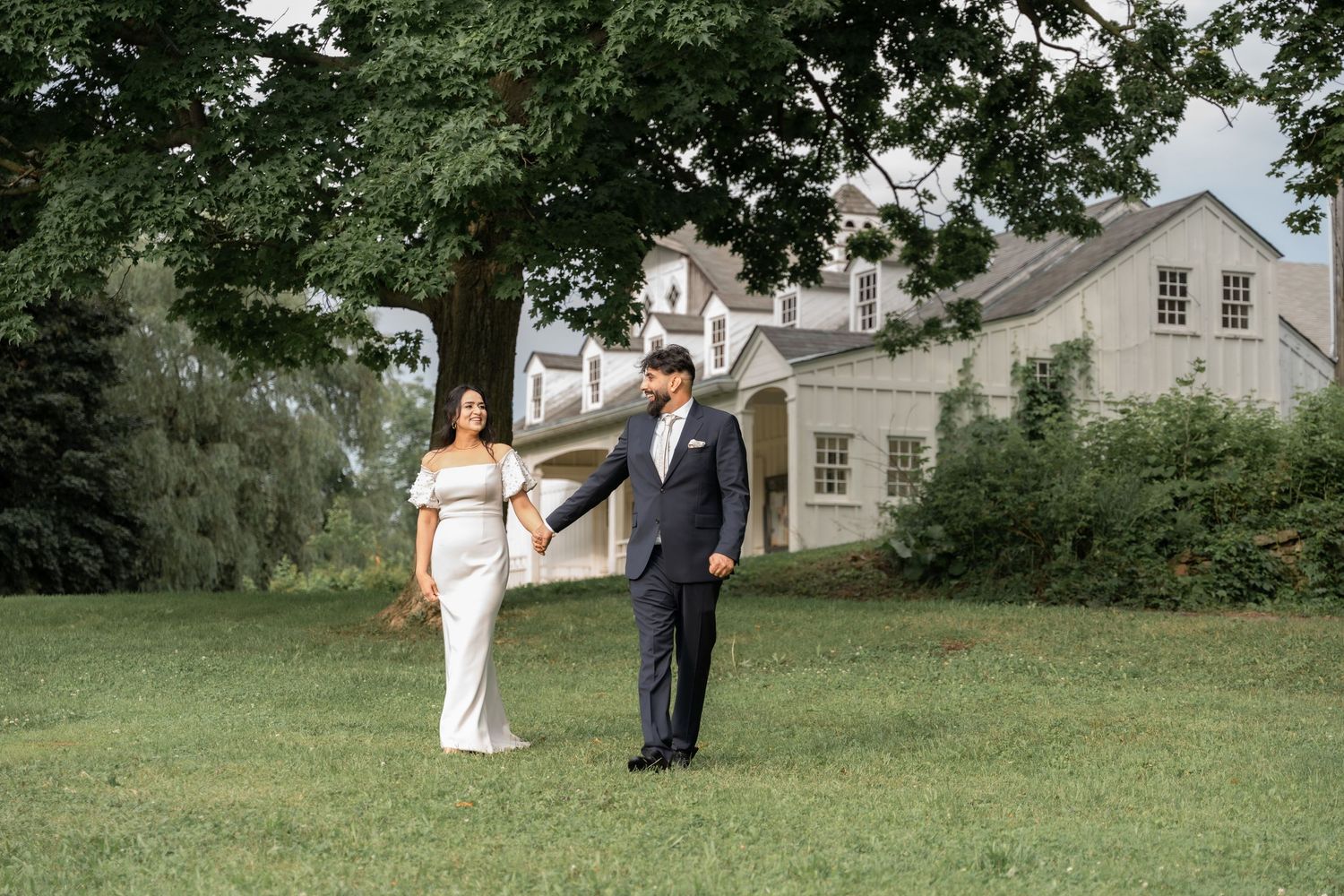 A couple in wedding attire walks together across a lush green lawn on their special day.