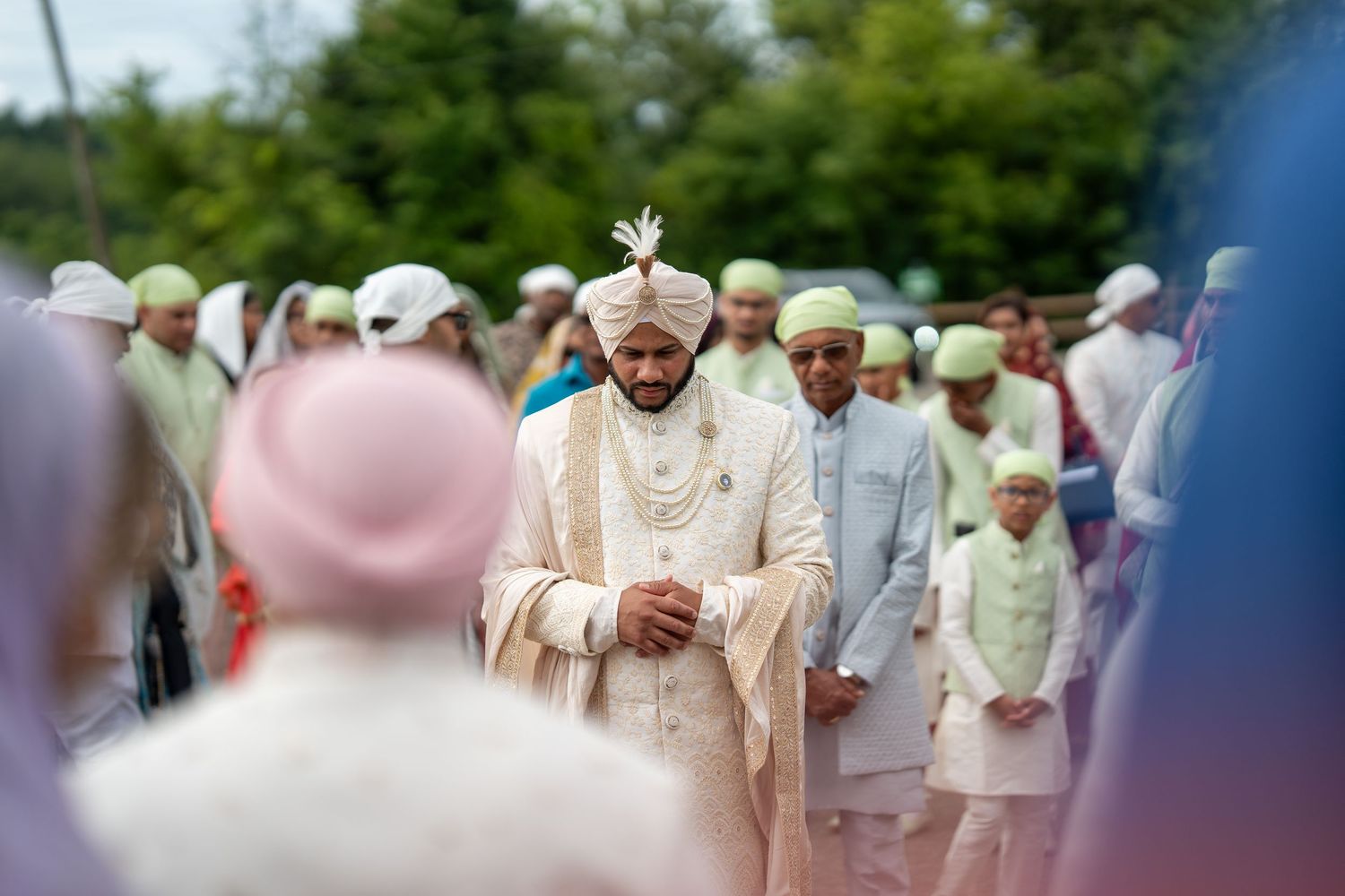Wedding procession outdoors with guests in traditional attire walking along a path.
